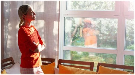 woman wearing orange shirt looking out of window towards yard