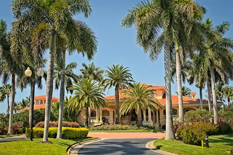 Tropical mansion with red-tiled roof surrounded by palm trees and lush landscaping
