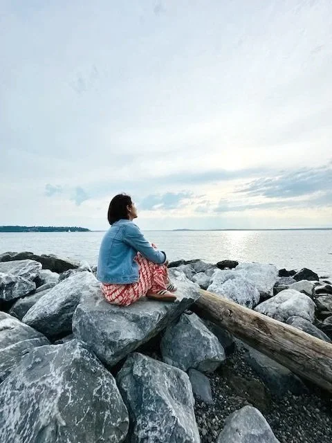 A woman on the shore staring at the ocean.