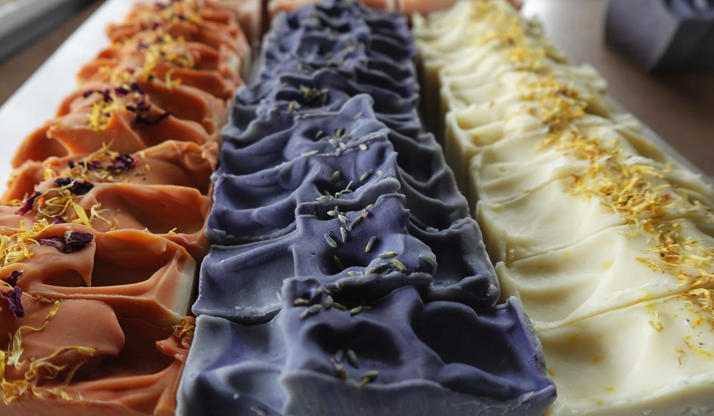 Colorful soap bars with floral and herb decorations arranged in rows.