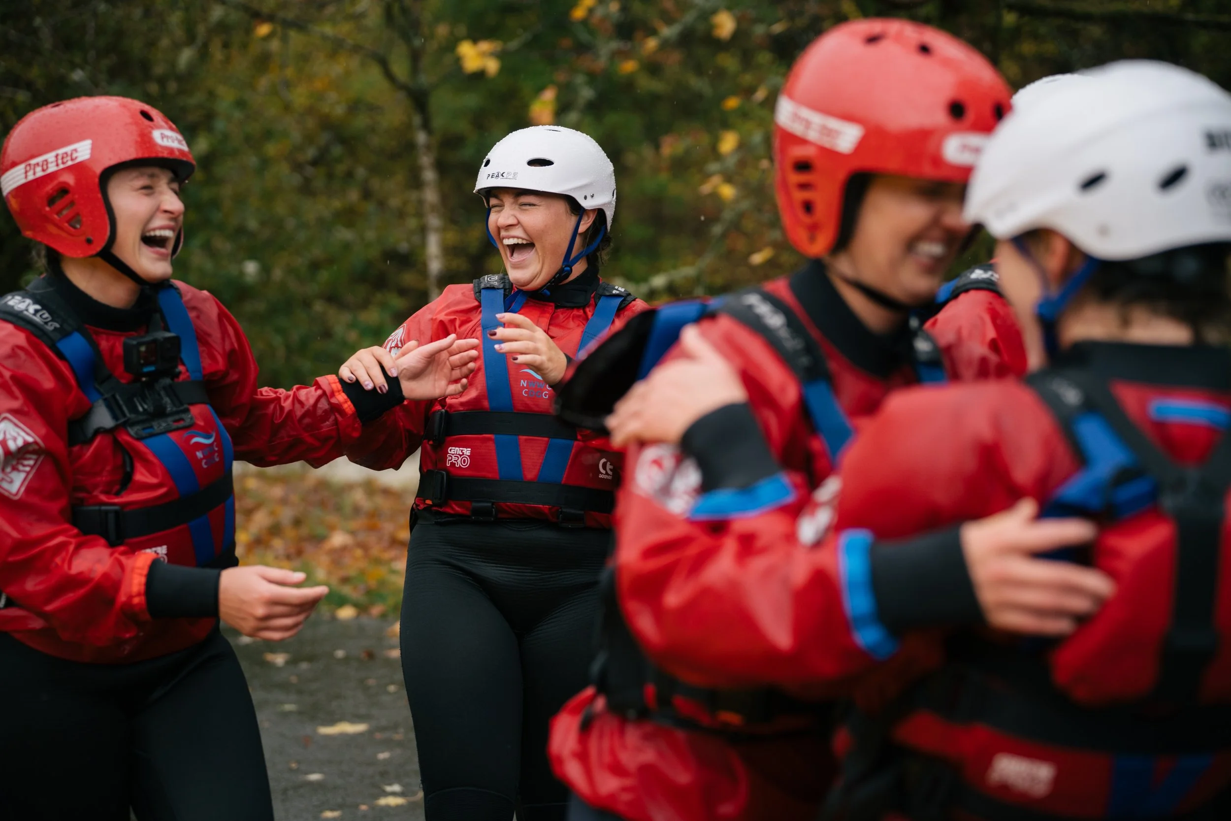 A group of people wearing helmets and red jackets, smiling and running outdoors with a forest background.
