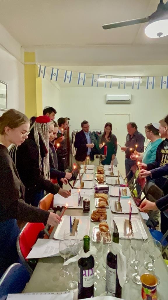 People gathered around a table with food, candles, and menorahs, celebrating Hanukkah.