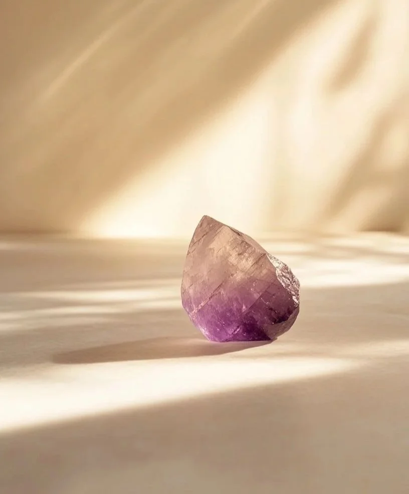 A purple and pink mineral gemstone on a white surface with soft lighting and shadows.