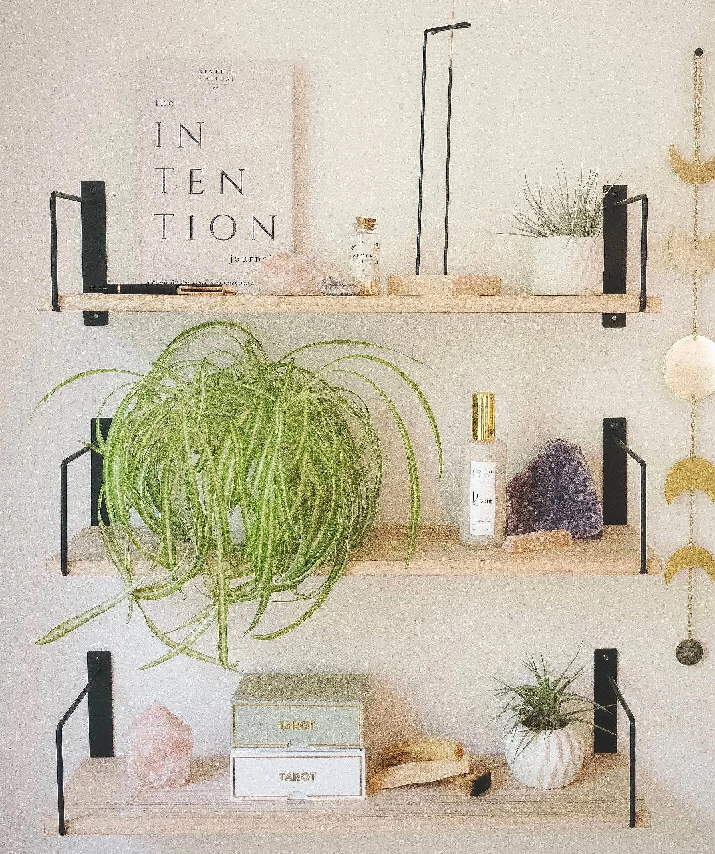Decorative wooden wall shelf styled with houseplants, crystals, tarot card boxes, and minimalist home décor.