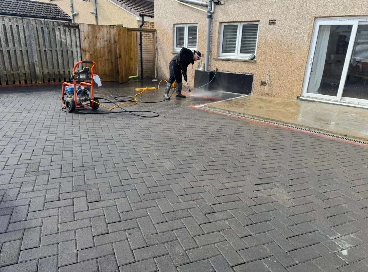 Person pressure washing a patio outside a house with a power washer.