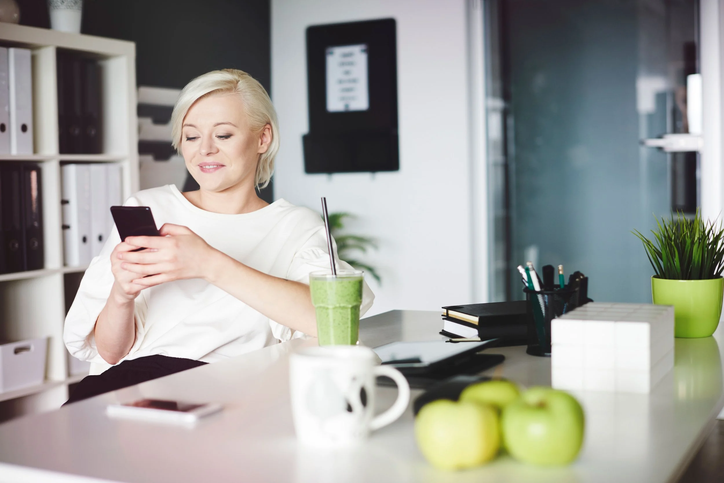 Professional woman with green smoothie booking appointment on her phone