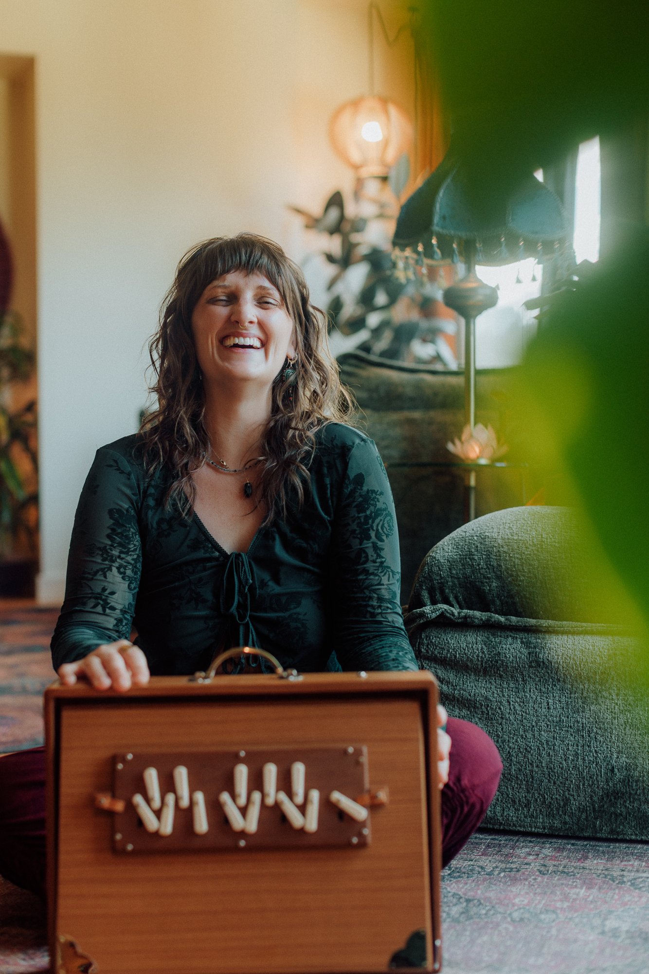 Emily Rose Meredith, somatic practitioner in Portland, Oregon, seated on a rug with a wooden shruti box in her healing space