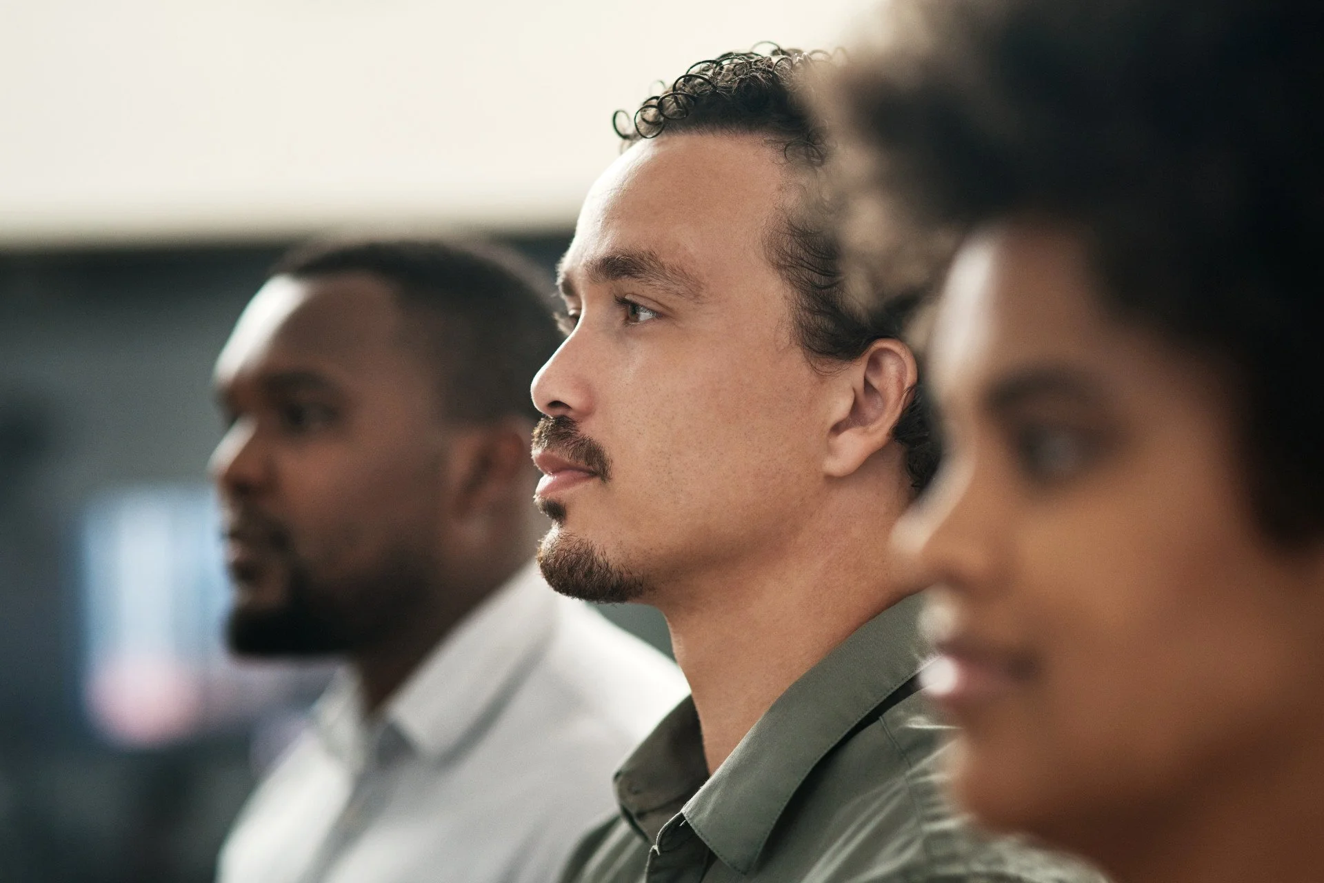 Three diverse professionals sitting in a row, listening attentively during a meeting.