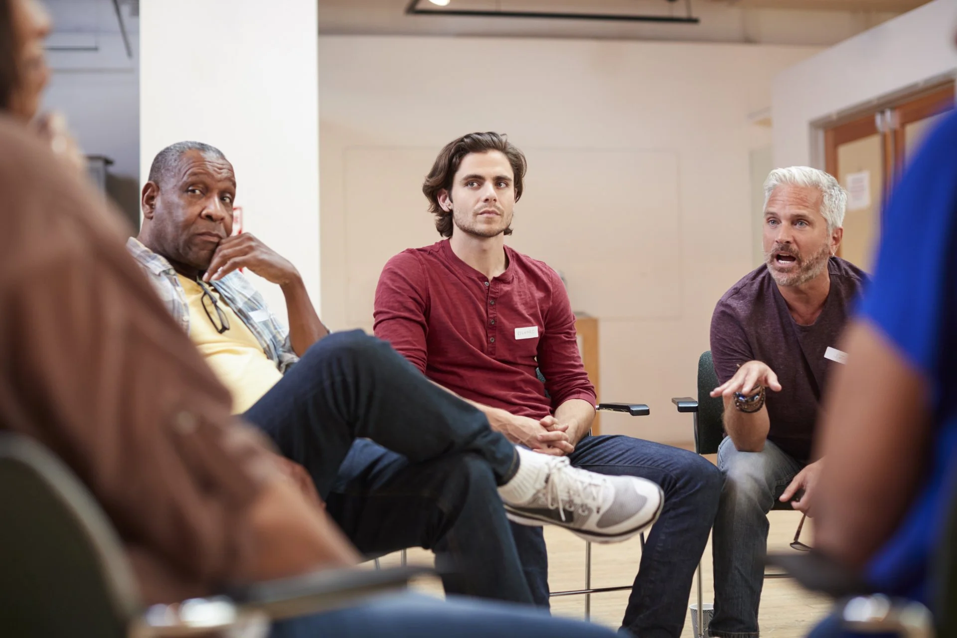 Group of diverse people participating in a discussion or support group meeting in a community center or classroom setting.
