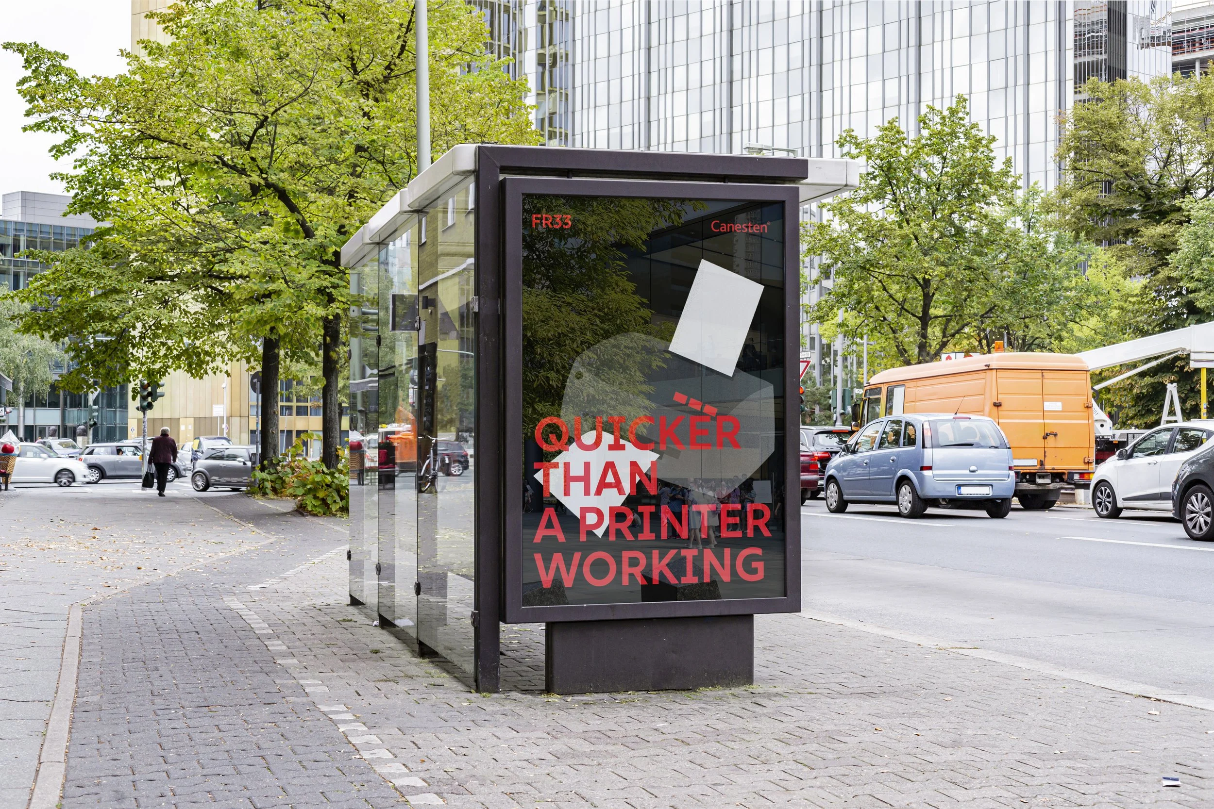 A city street scene with a bus stop shelter containing an advertisement for printers, with a background of trees, modern glass buildings, and cars parking and driving on the street.