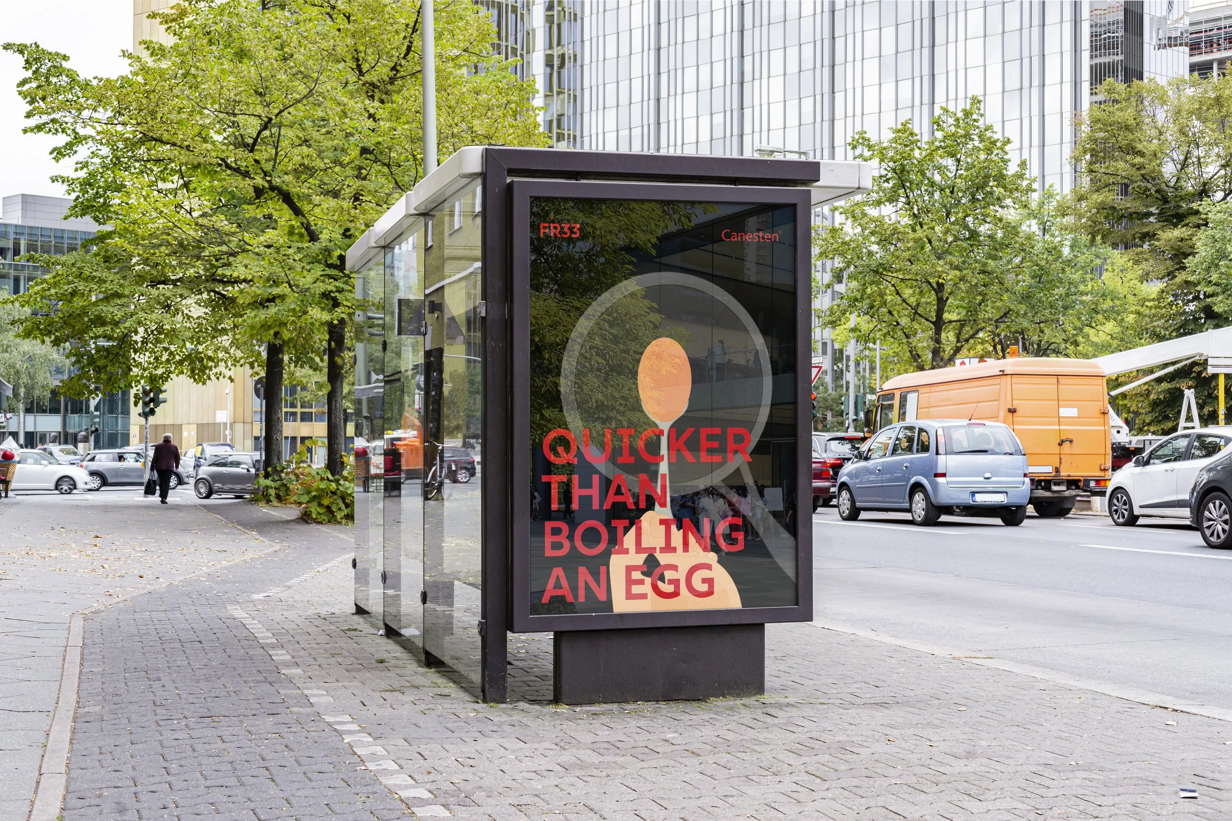 City street scene with a bus shelter advertising, trees with green leaves, modern glass office buildings, parked cars, and people walking.