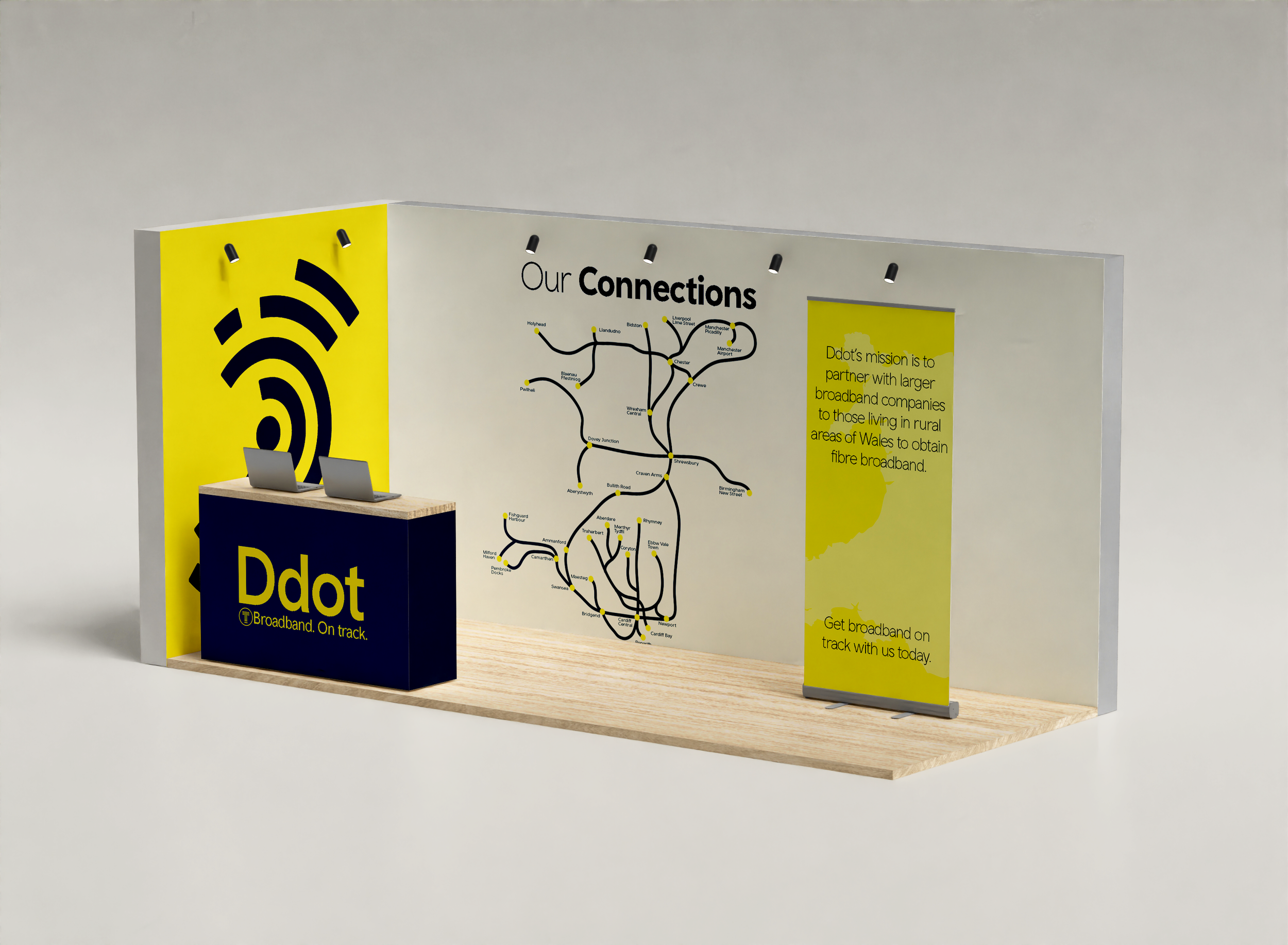 An exhibition display for Ddot, a broadband company, features a yellow and navy booth with a large Wi-Fi symbol on the yellow side panel. There is a wooden table with two laptops and a white partition with the title 'Our Connections' displaying a map and information about partner broadband services in Wales. A yellow roll-up banner on the right provides additional company information.