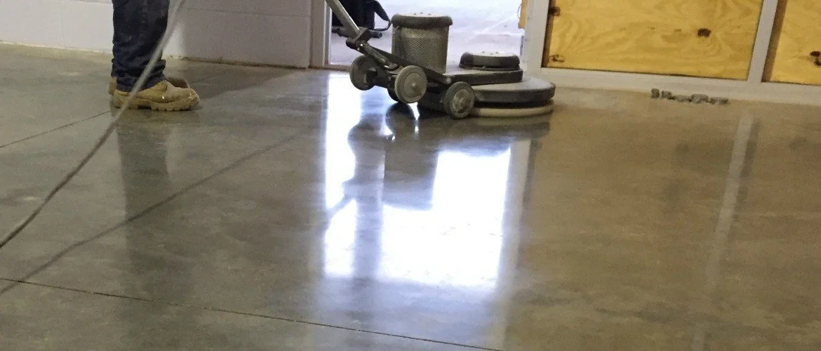 Person polishing a concrete floor with a floor buffer machine in a construction area.