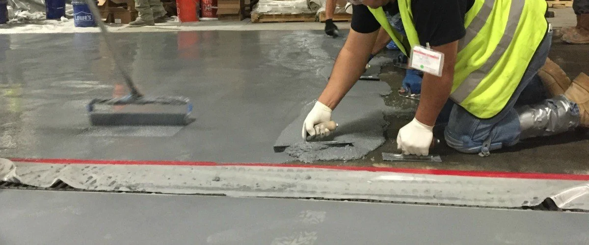 Worker applying gray concrete or cement with a trowel at a construction site.
