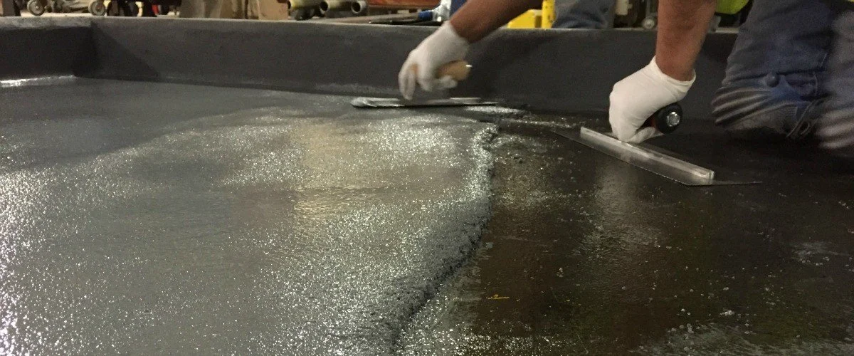 Workers wearing gloves smoothing a black, glossy surface with a trowel.