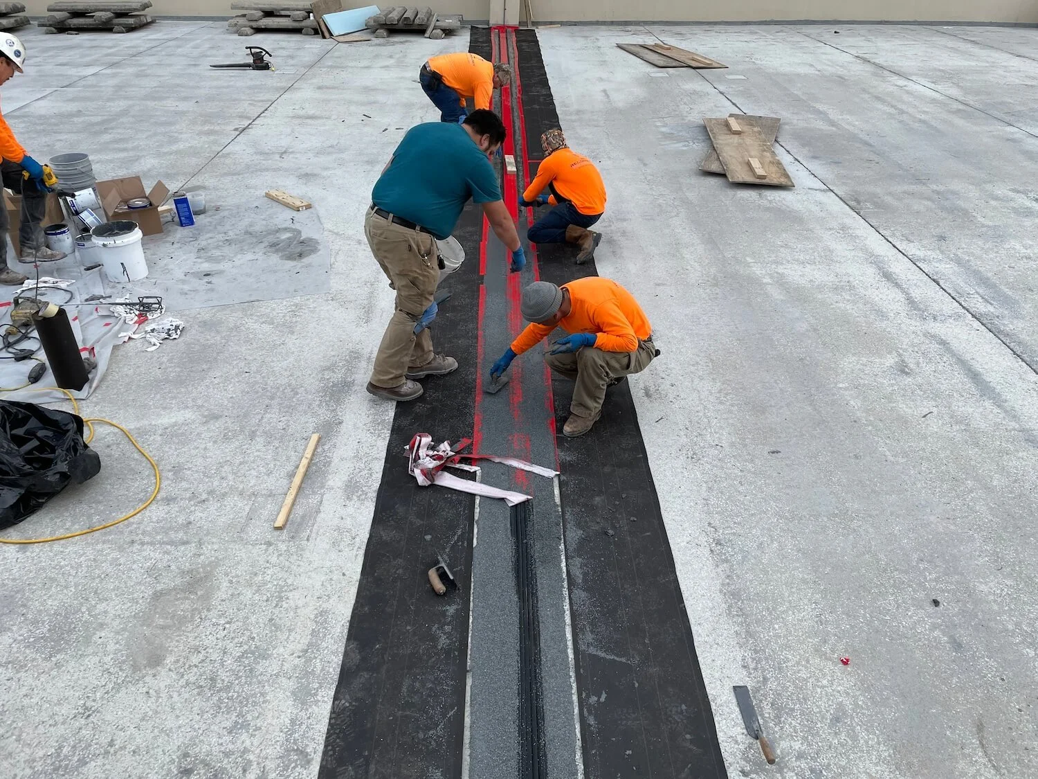 Construction workers installing or repairing a track embedded in a concrete surface, with tools and materials around them.