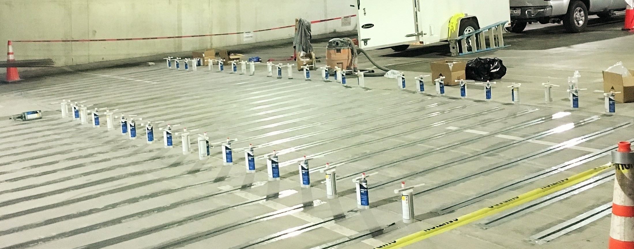 Underground parking garage with heating pipes installed on the floor, along with tools, supplies, and cones for construction or maintenance work.