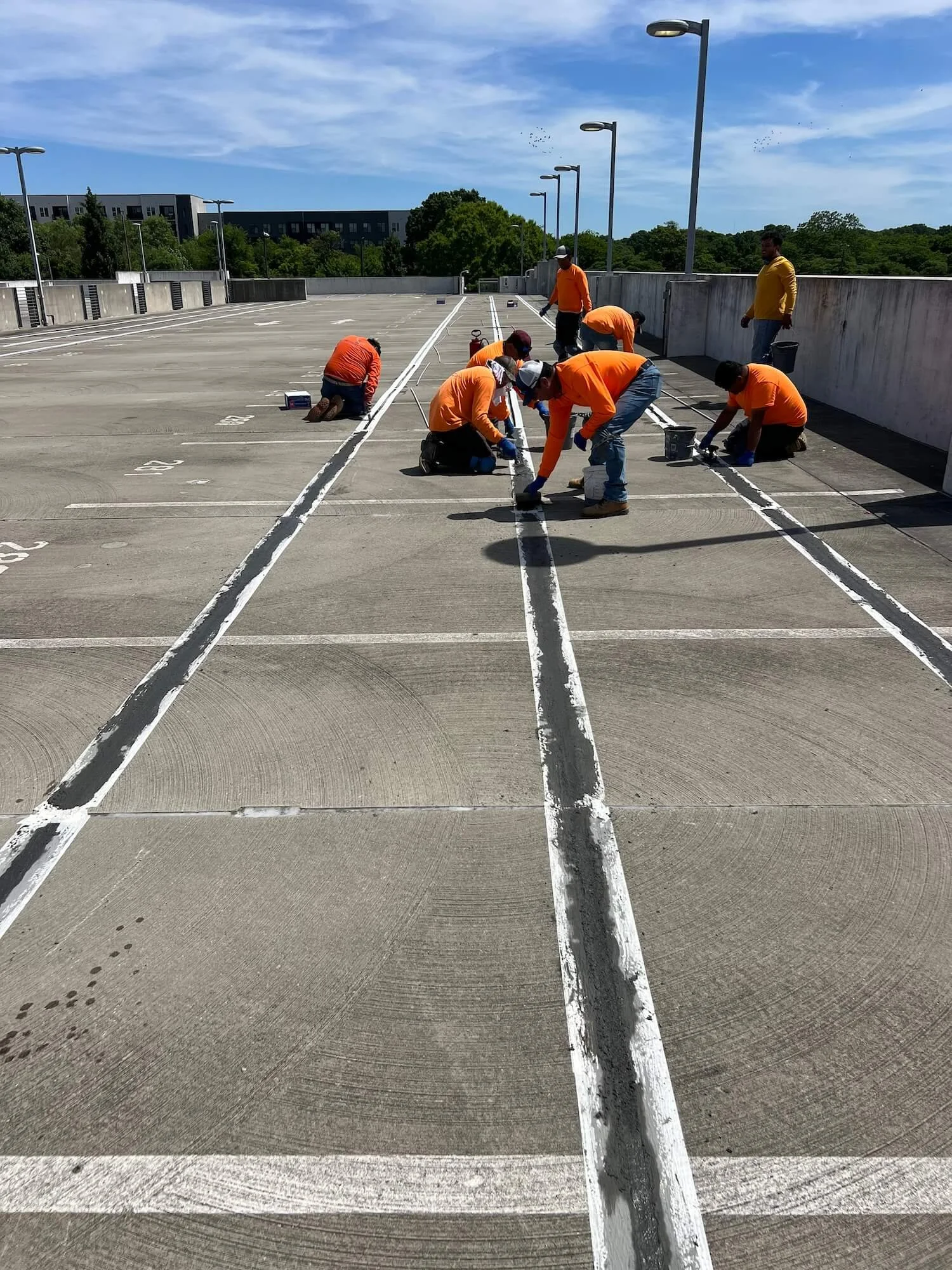Workers in orange shirts painting parking lot lines.