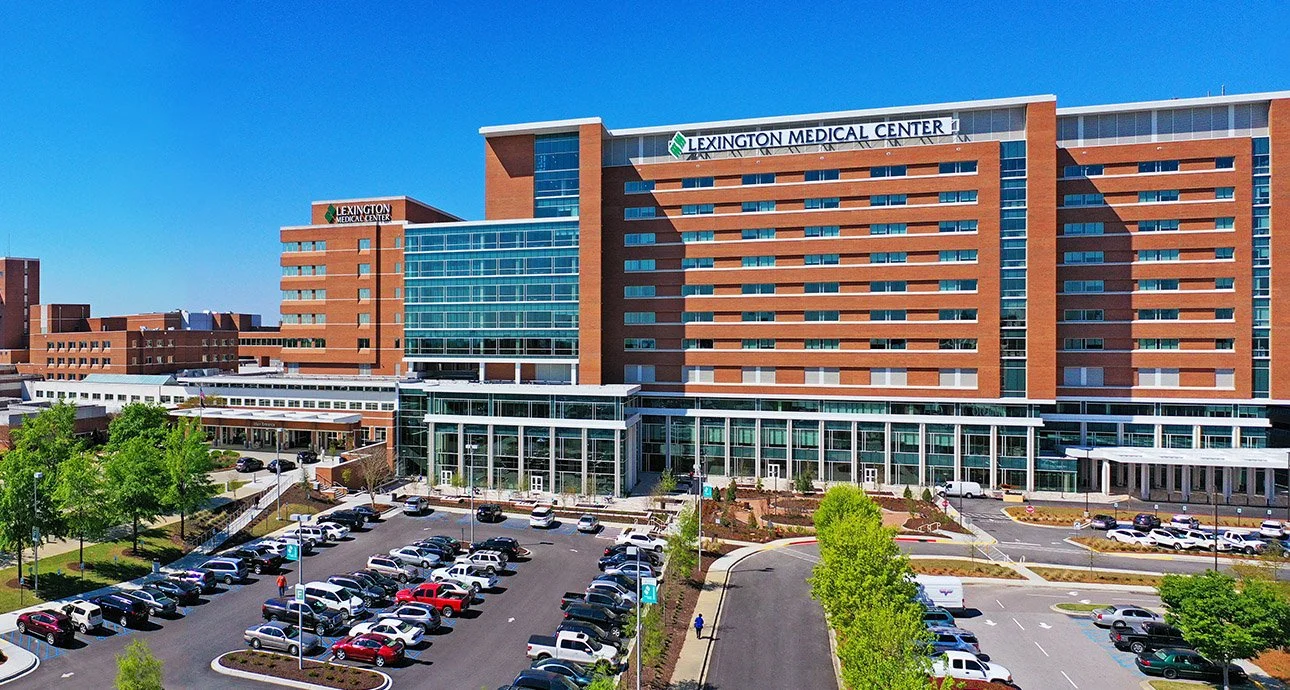 Exterior view of Lexington Medical Center hospital with parking lot and landscaping under a clear blue sky.