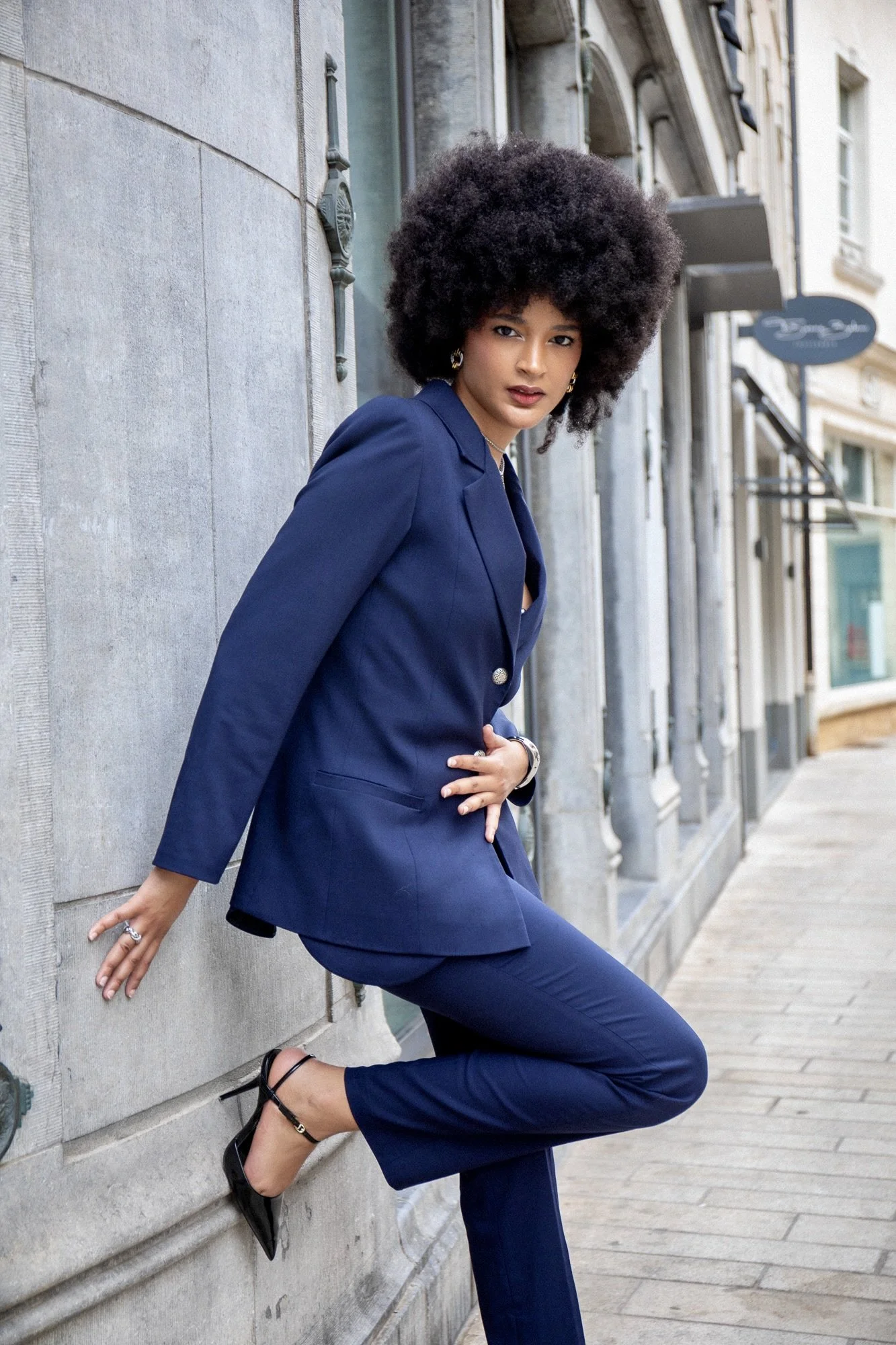 Full-body fashion editorial of model Ana wearing an elegant blue tailored suit by Francini_K, styled with Ennomerato jewelry. Photographed by Henri Da Cruz in the streets of Luxembourg, featuring a dynamic pose, contemporary tailoring and sophisticat