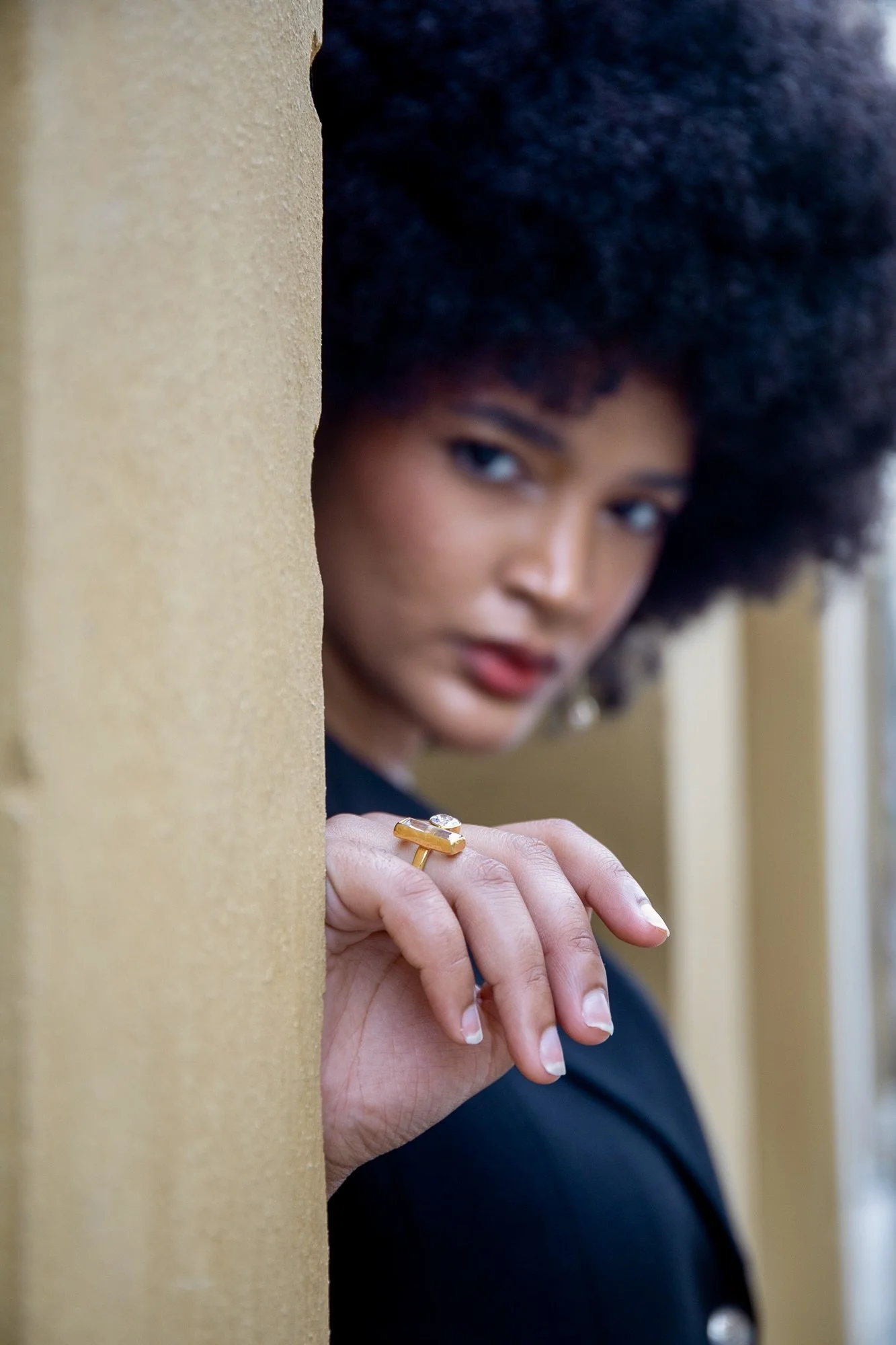 Creative jewelry editorial featuring a gold statement ring by Ennomerato, with model Ana softly blurred in the background. Fashion styling by Francini_K, photographed in Luxembourg by Henri Da Cruz.