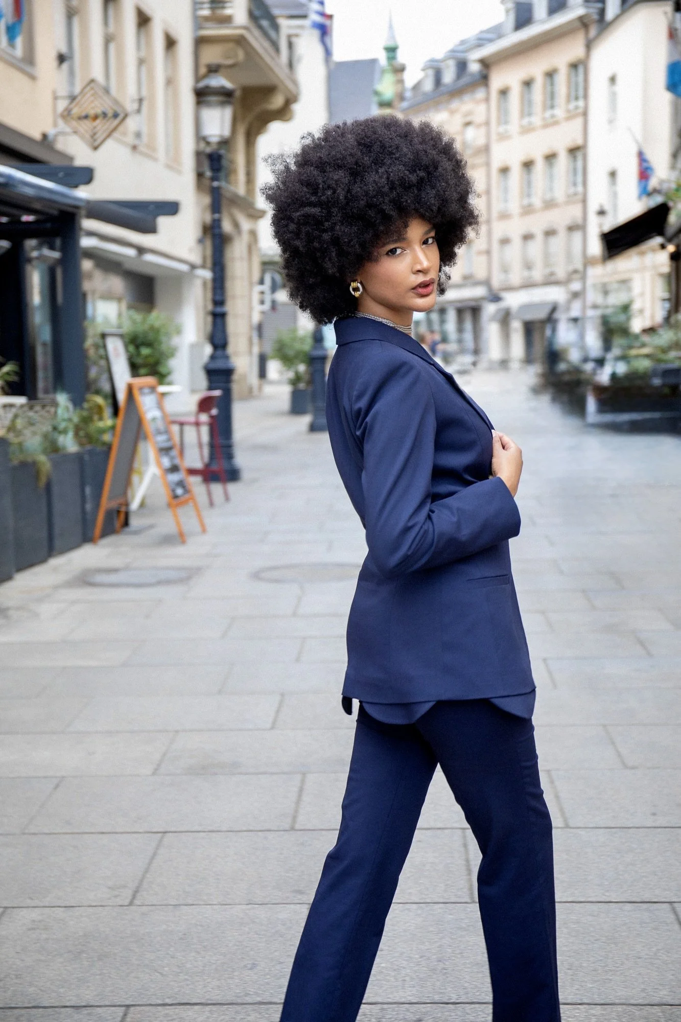 Fashion editorial photographed by Henri Da Cruz in Luxembourg City, featuring model Ana wearing a blue tailored suit by Francini_K. A confident side pose highlights the elegant silhouette and contemporary tailoring, combining sophisticated street sty