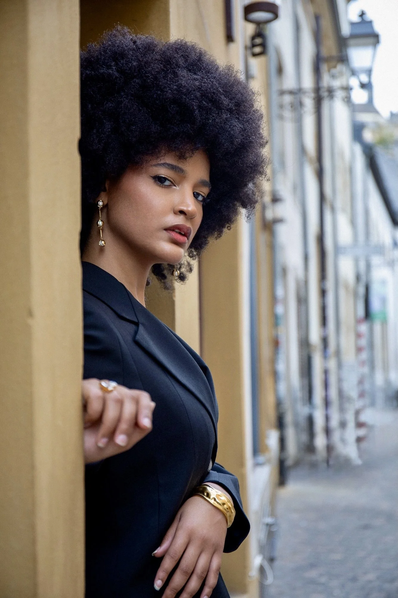 Fashion and jewelry editorial in Luxembourg featuring model Ana wearing a black tailored suit by Francini_K and gold jewelry by Ennomerato. Photography by Henri Da Cruz.