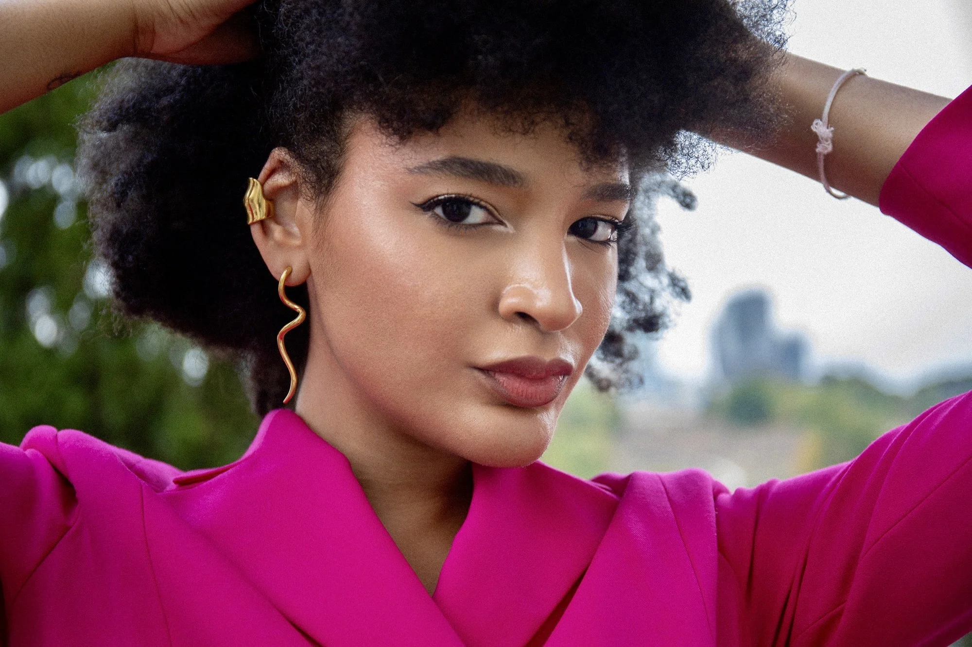 Close-up fashion portrait of model Ana wearing a vibrant fuchsia blazer by Francini_K, photographed by Henri Da Cruz in Luxembourg. A confident gaze, sculptural hairstyle and elegant gold earrings create a striking contemporary fashion editorial.