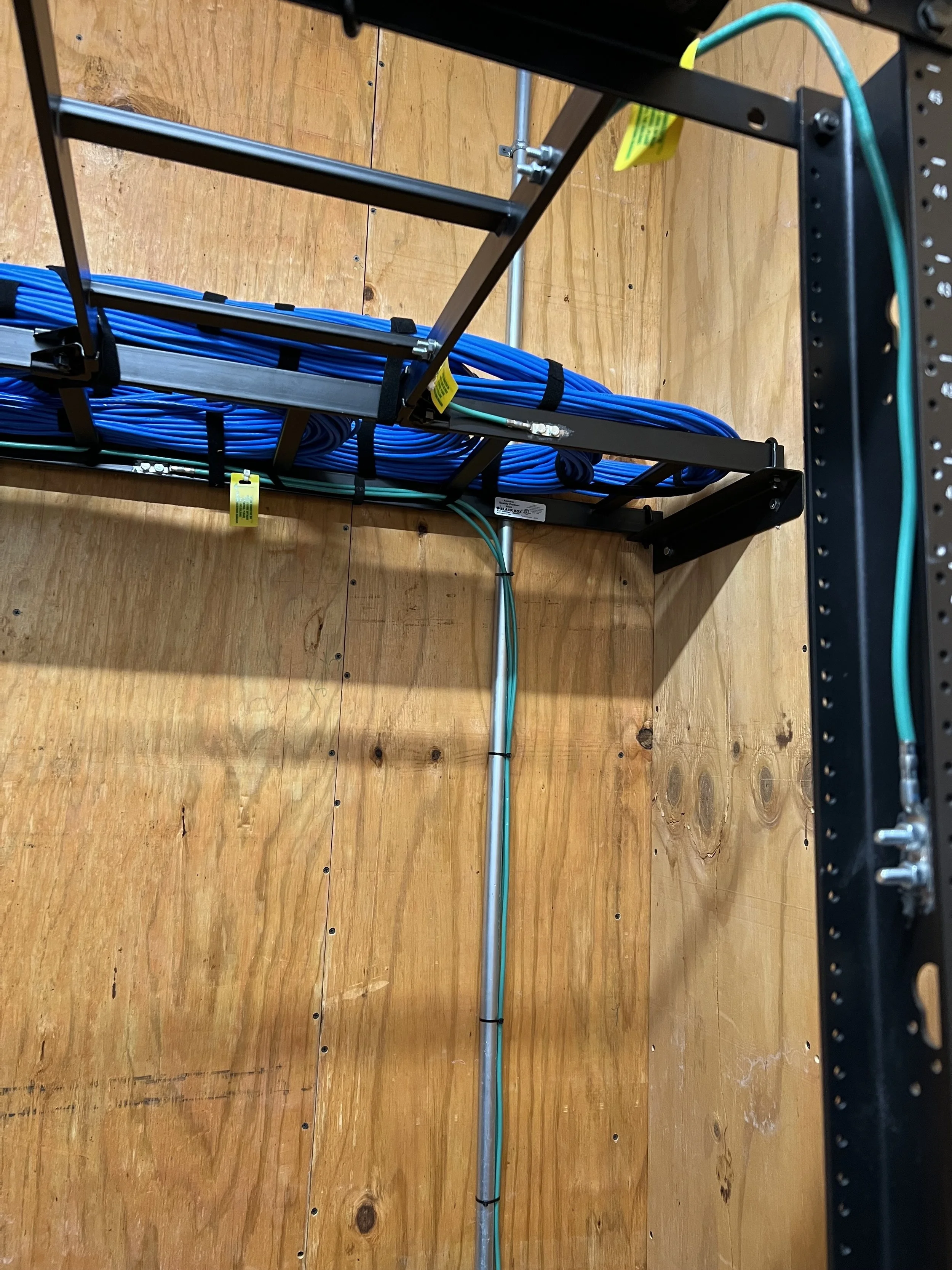 View of a network rack with blue Ethernet cables, mounted on a wooden wall or floor.