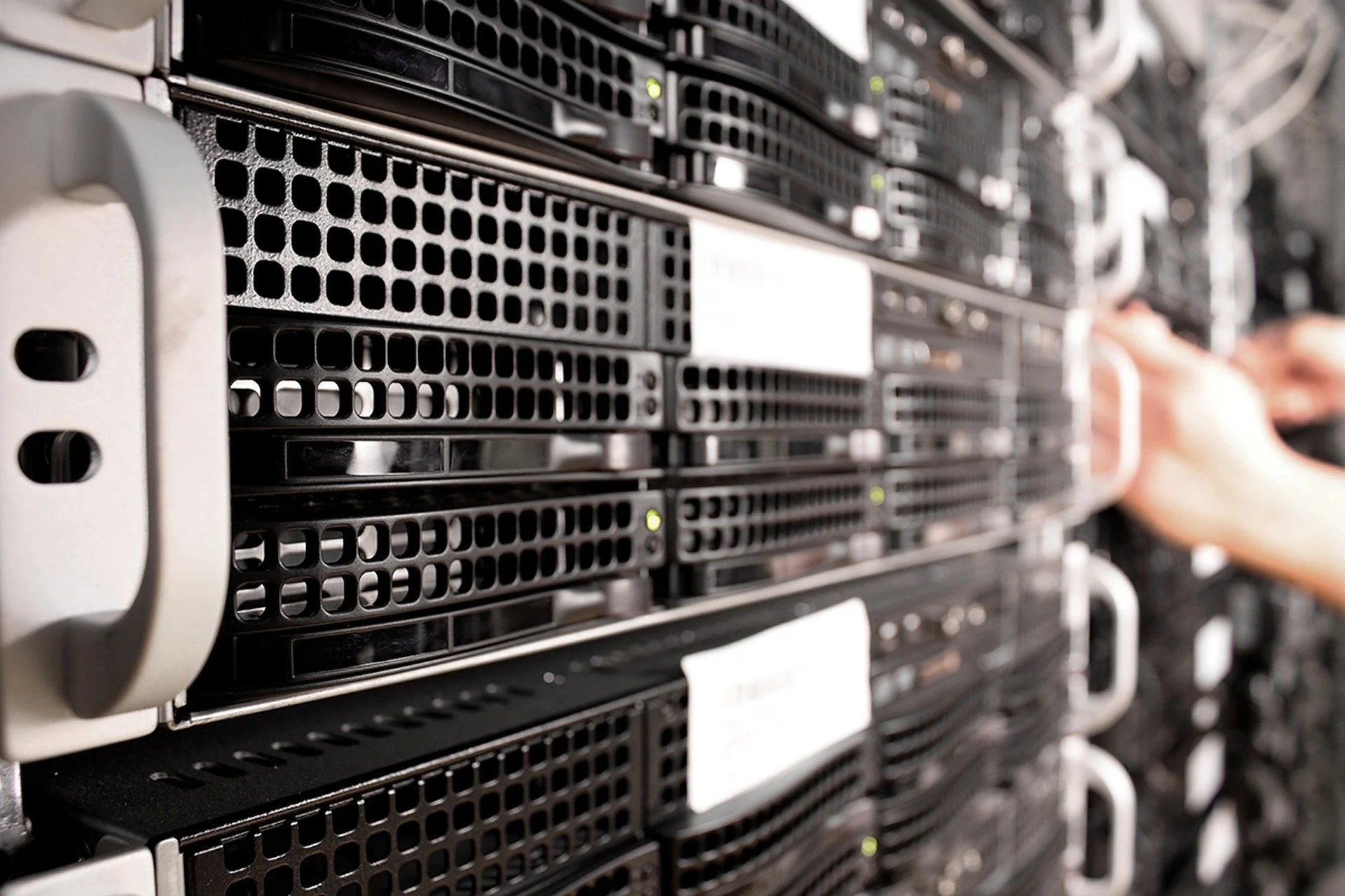 Server racks in a data center with a person's hand adjusting a component.