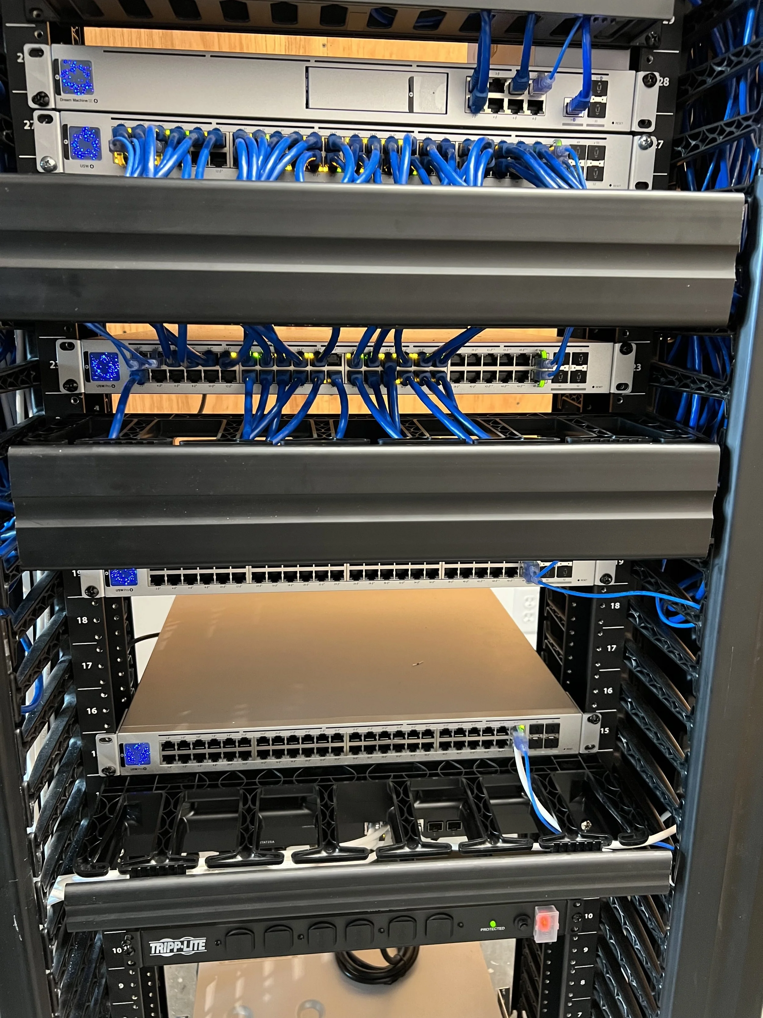 A server rack with multiple network switches and blue Ethernet cables connected to them, situated in a data center or network room.