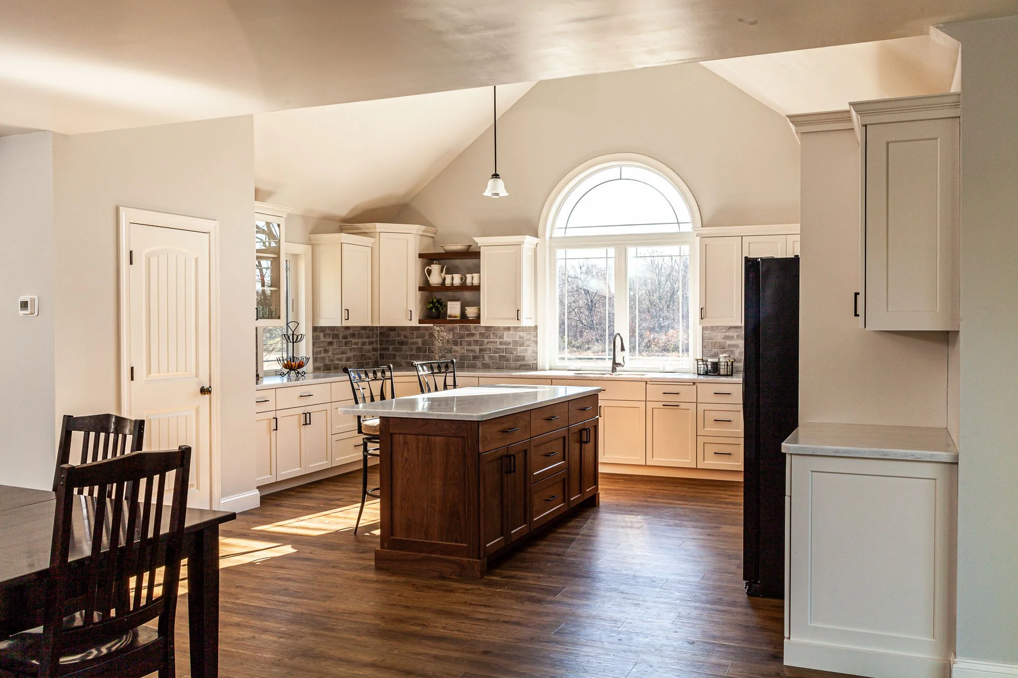Bright modern kitchen with white cabinets, a large window, and a central wooden island.