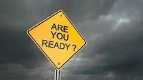 Yellow diamond-shaped sign asking 'Are you ready?' against dark cloudy sky.