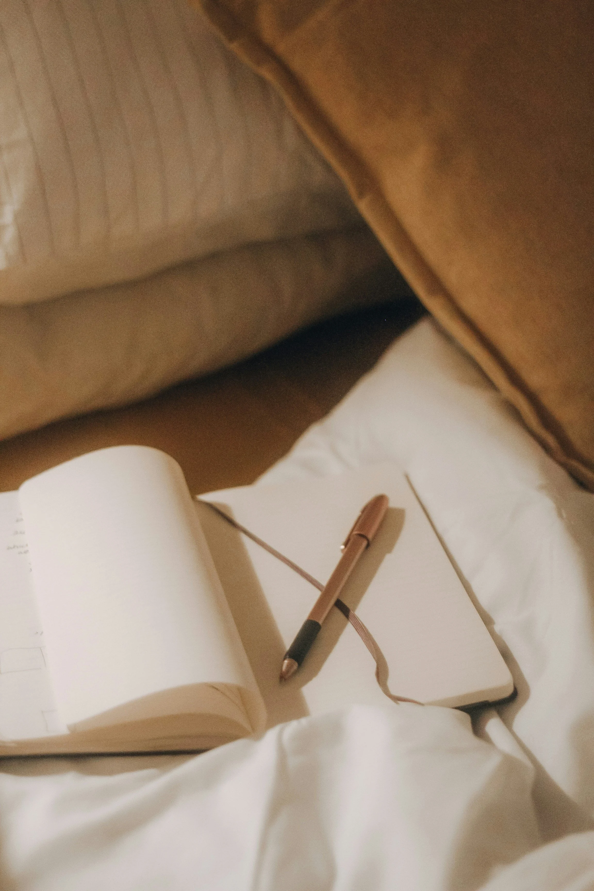 Open notebook with blank pages, a rose gold pen, and a brown cable on a white fabric surface.