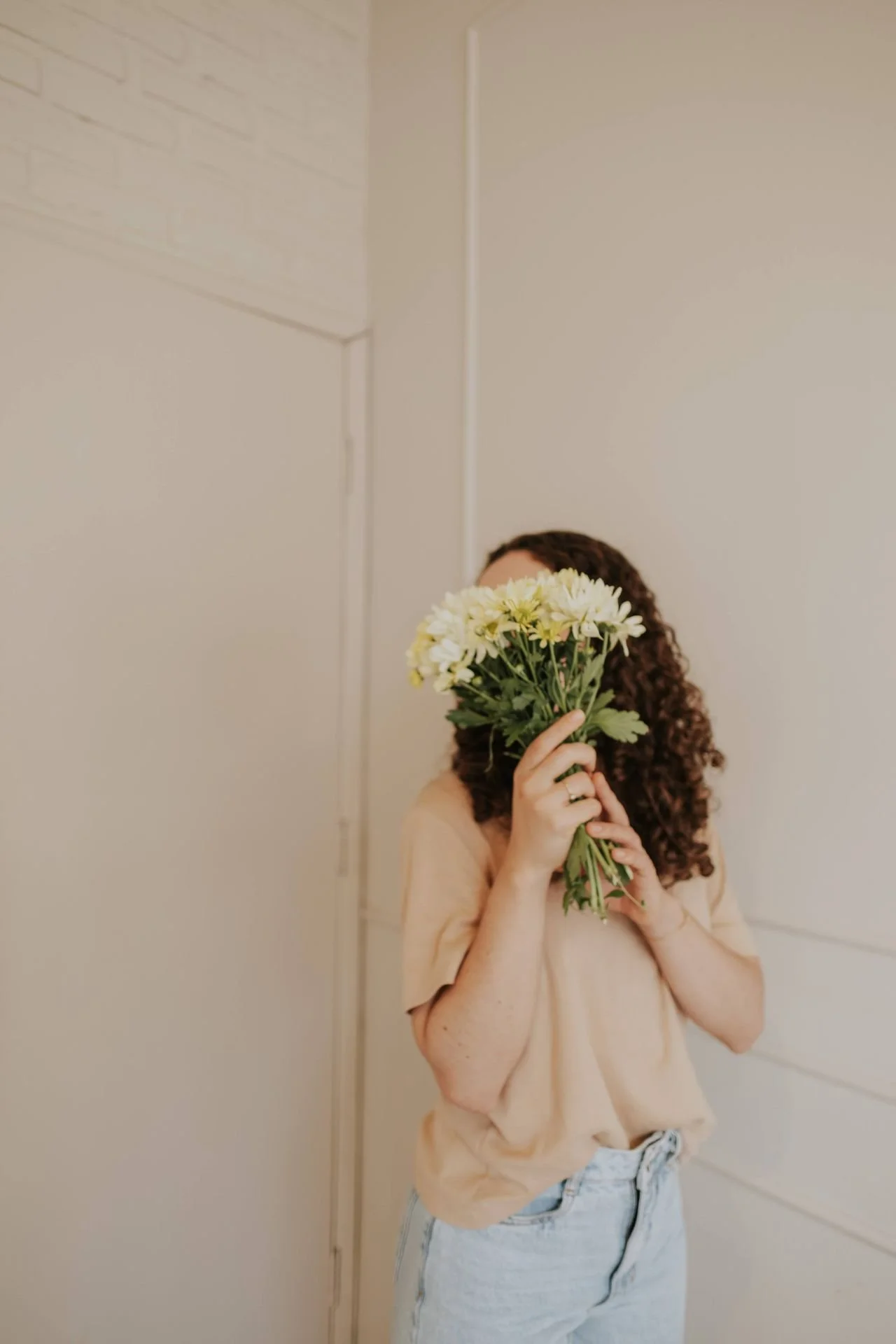 A woman holds a bouquet of flowers up blocking her face as she stands in an empty room