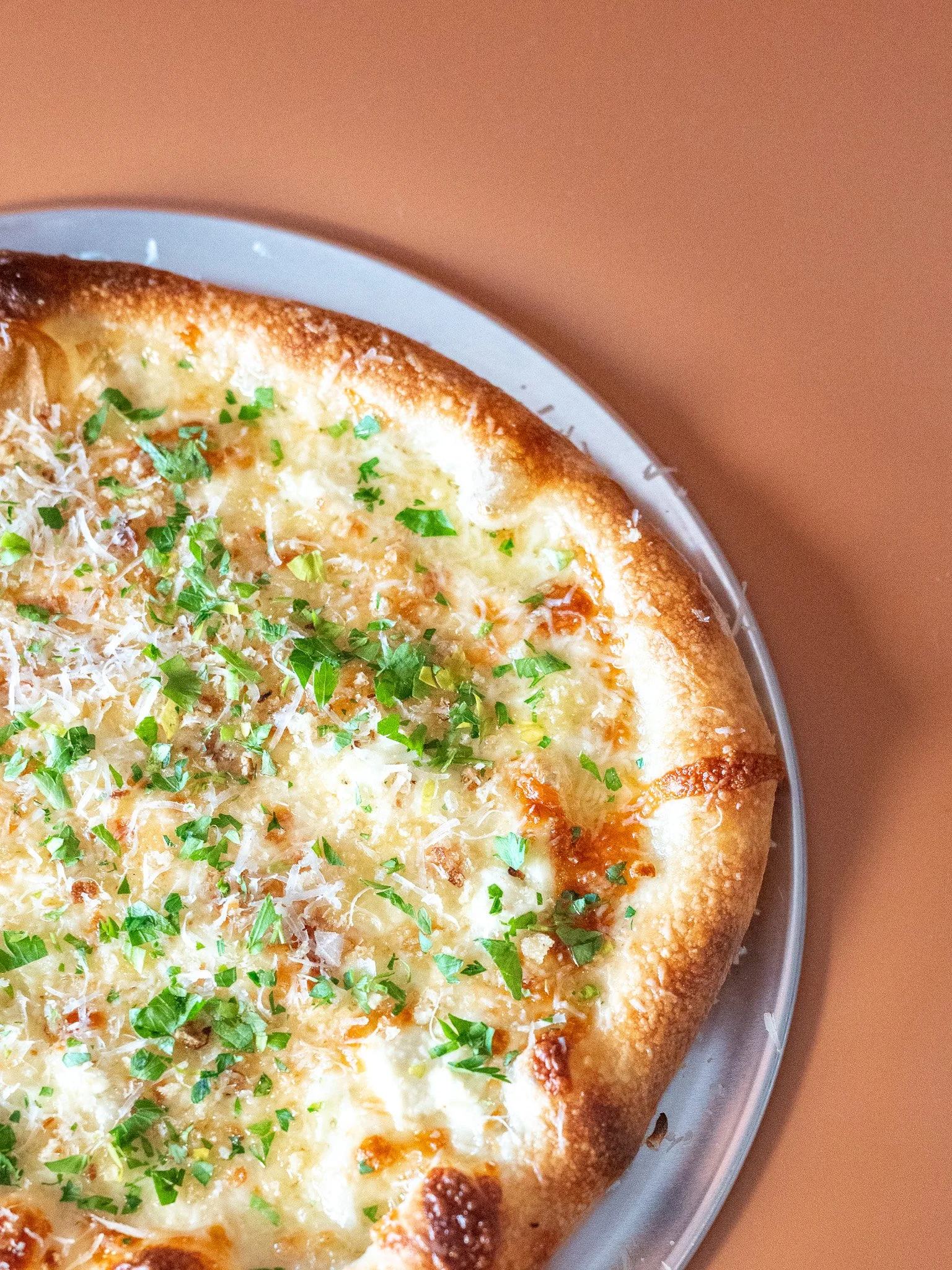 Close-up of a cheese pizza topped with green herbs and grated cheese, in a glass dish.