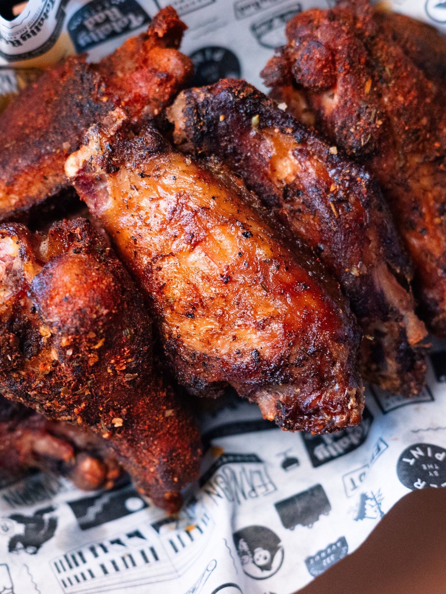 Close-up of seasoned and cooked chicken wings resting on black and white printed paper.