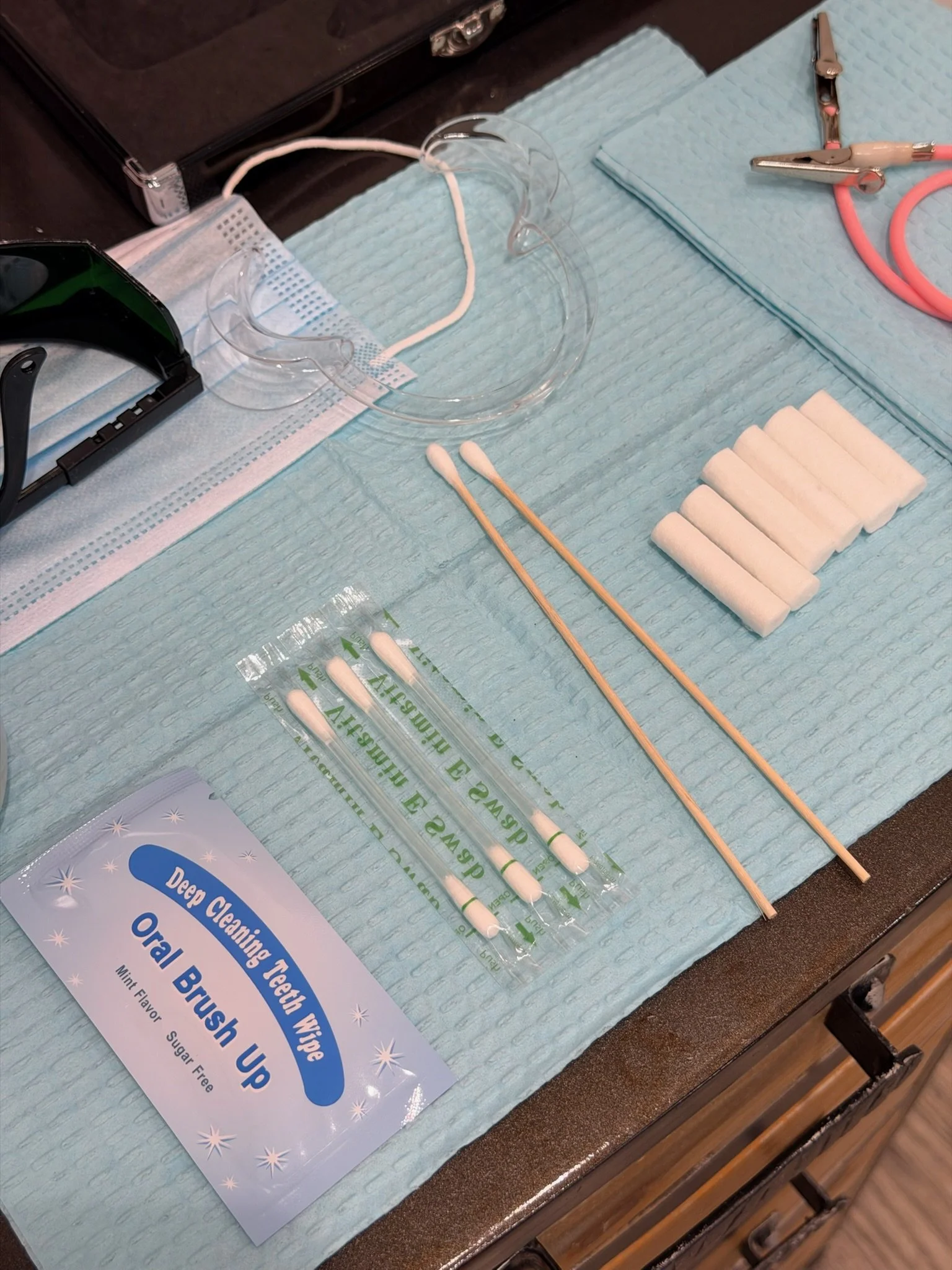 Medical tools and supplies on a table, including a face shield, cotton swabs, small foam pads, and a flyer about oral brushing.