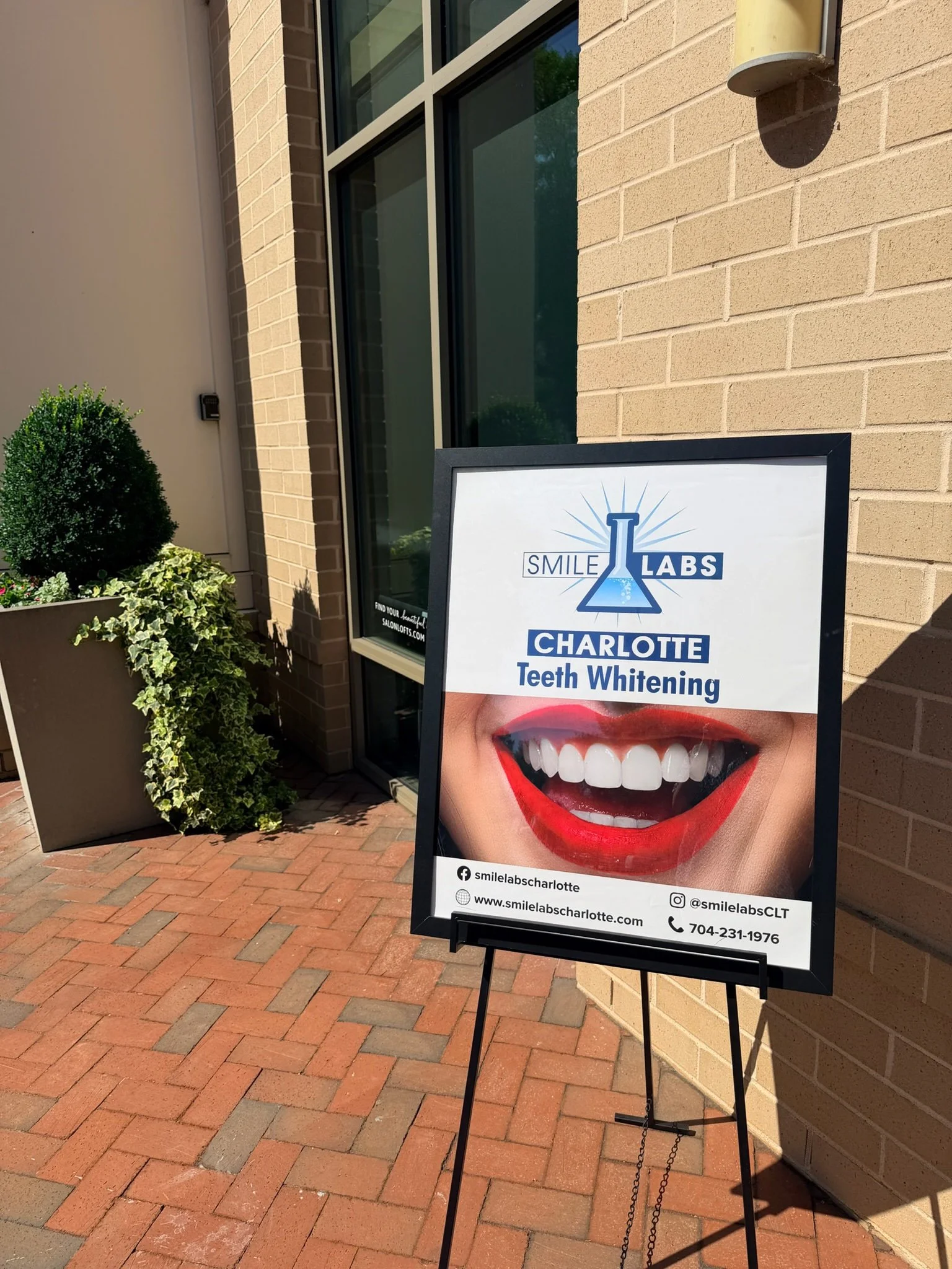 Sign advertising teeth whitening services at Smile Labs Charlotte, with a close-up photo of a bright, smiling mouth with white teeth.