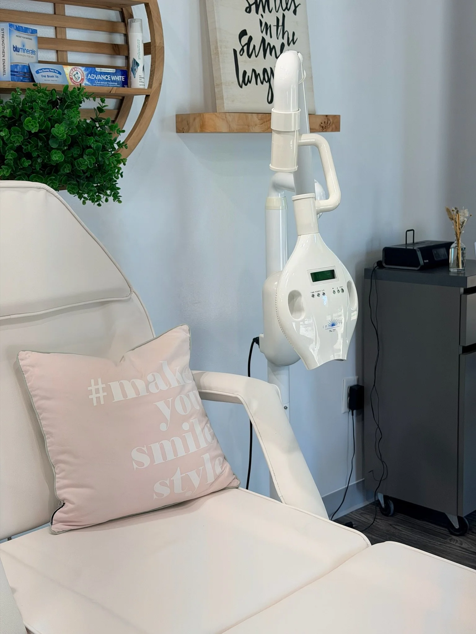 A white medical chair with a light pink pillow that has the hashtag #makeyousmilestyle on it. A piece of tooth whitening medical equipment is next to the chair.