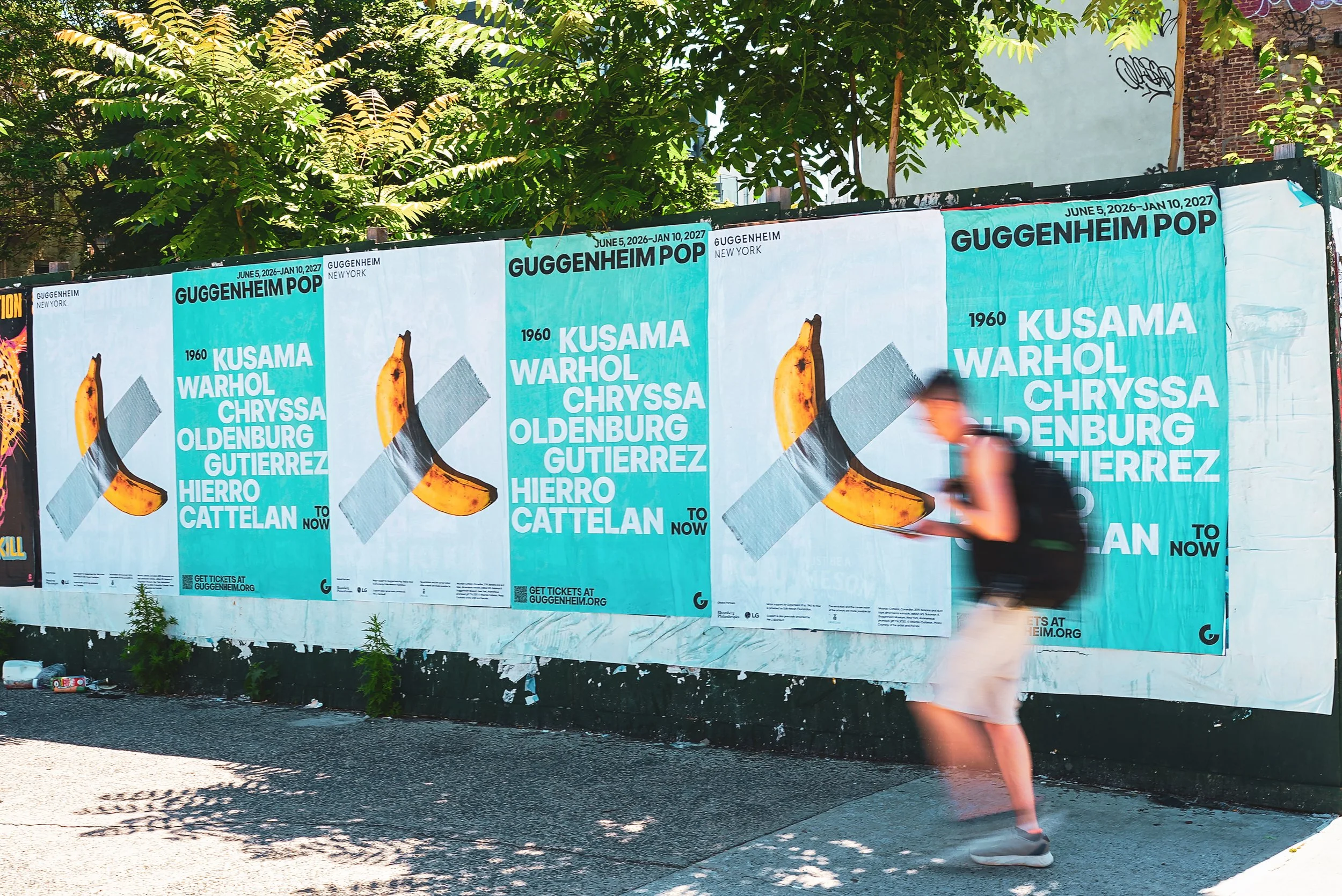Large blue wheatpaste posters advertising an event titled 'Guggenheim Pop' featuring artists Kusama, Warhol, Chryssa, Oldenburg, Gutierrez, Hierro, Cattelan, scheduled from June 5, 2026, to January 10, 2027, in New York.