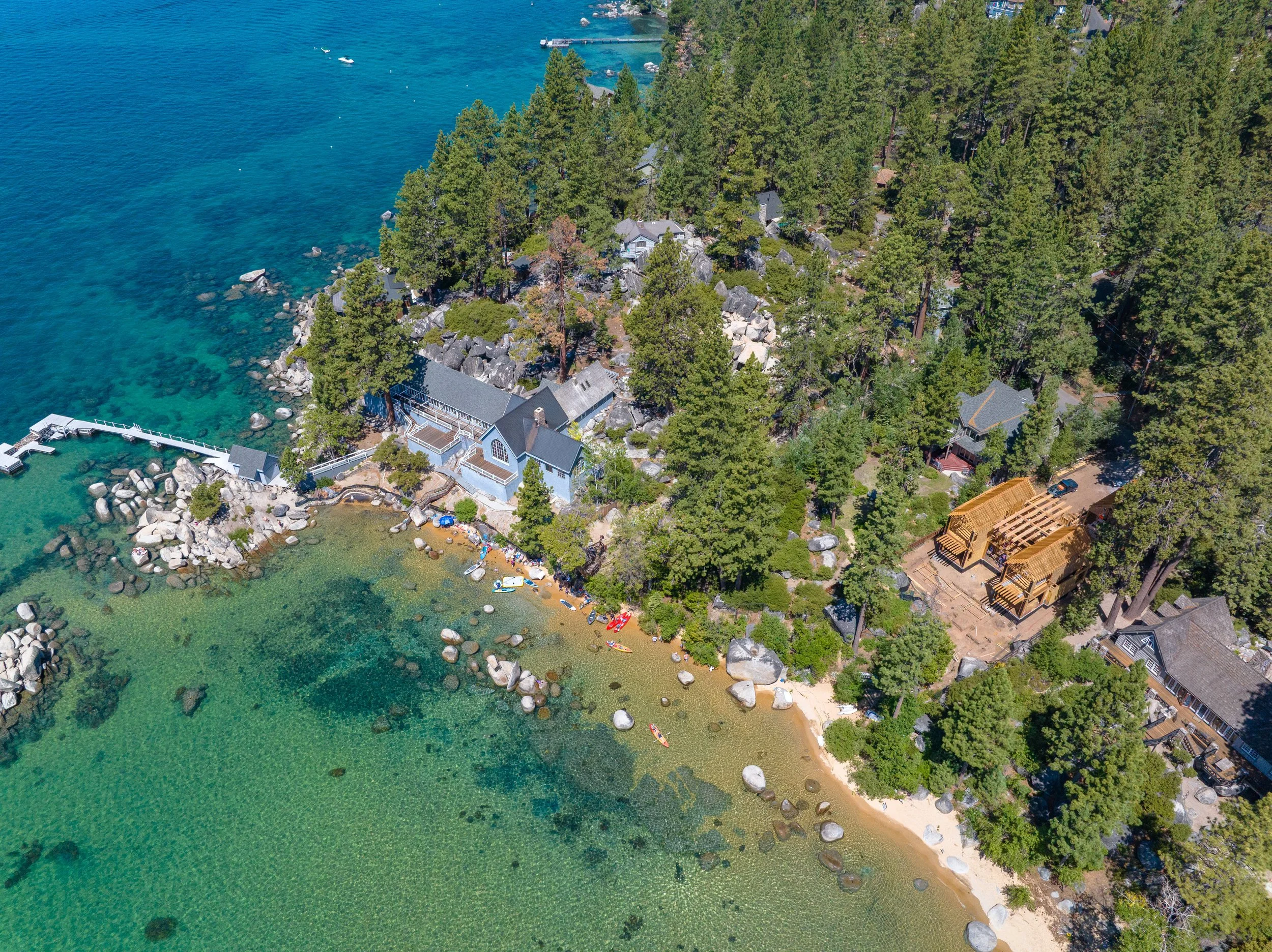 Aerial view of a lakeside with houses, trees, rocky shoreline, and boats on the water.