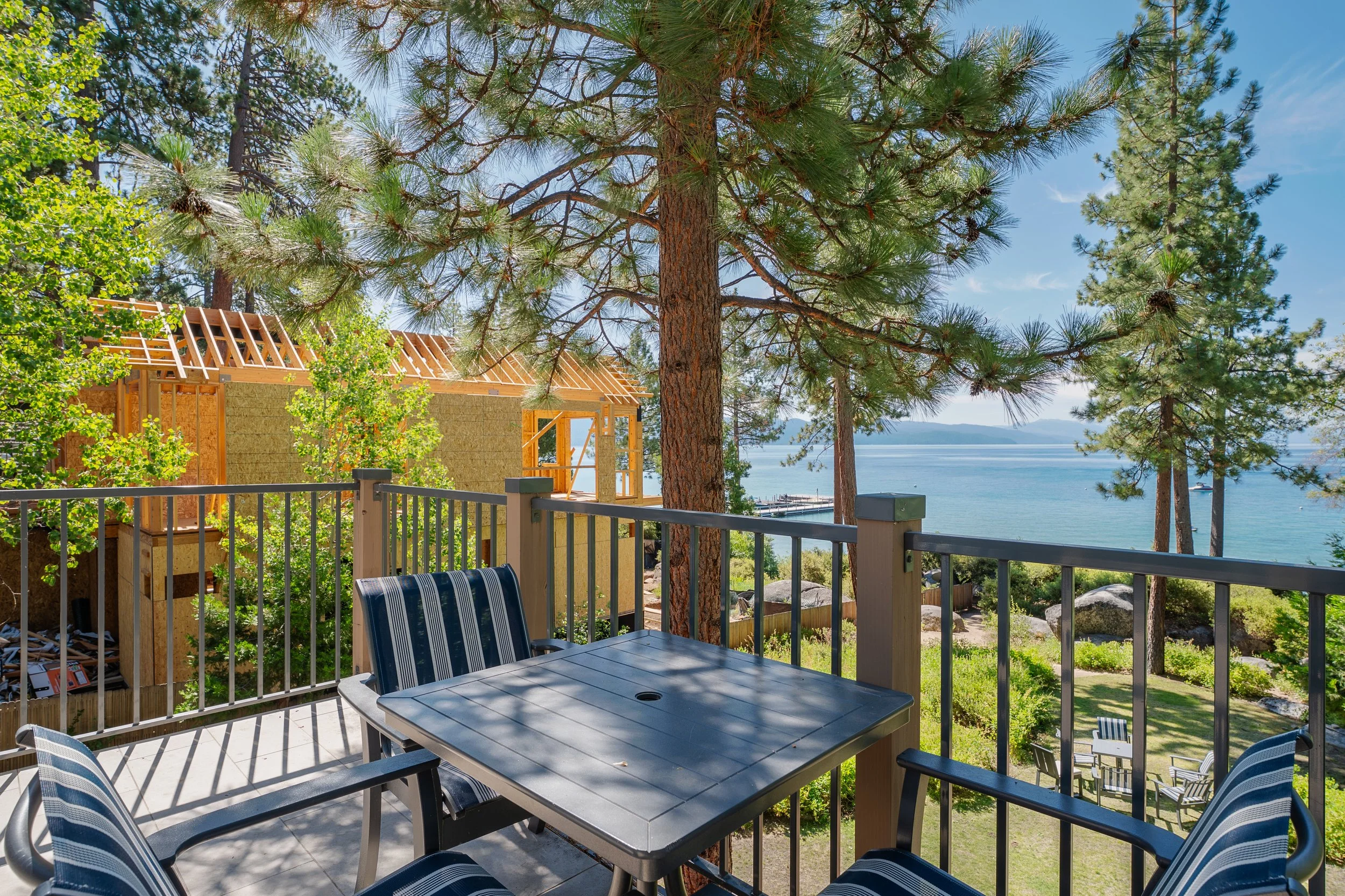 A view from a balcony overlooking a lake with trees and a partially built wooden house under construction.