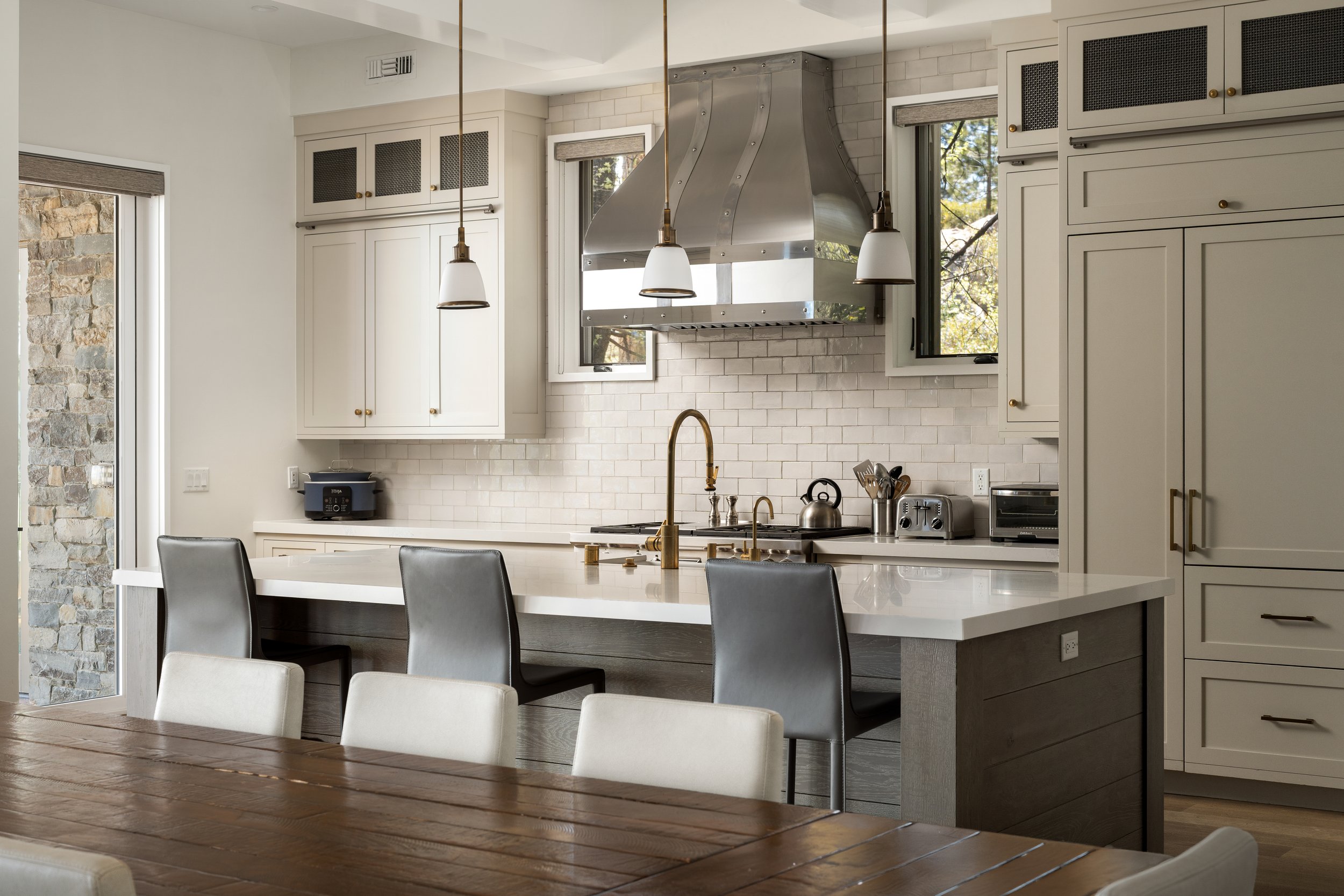 Modern kitchen with white cabinets, stainless steel range hood, black stovetop, pendant lights, and dining area with white chairs around a wooden table.