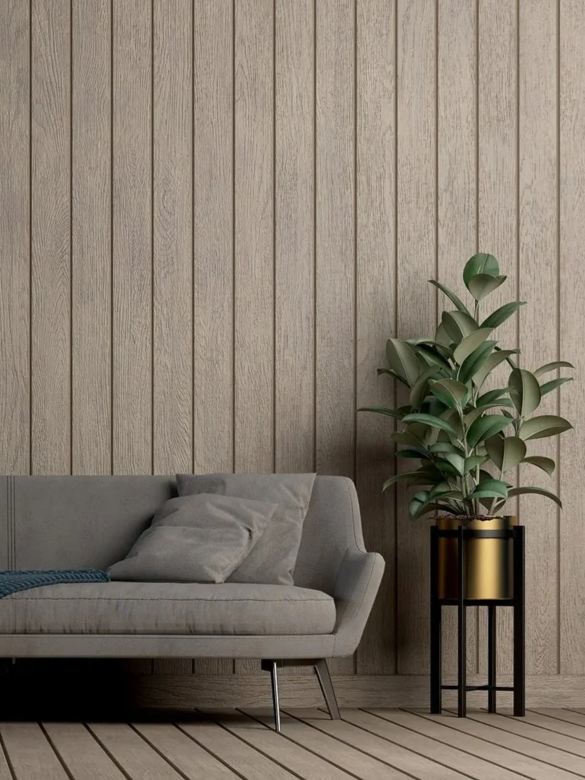 Living room with beige upholstered sofa, light-colored pillows, wooden wall paneling, and a large potted plant in a black and gold stand.