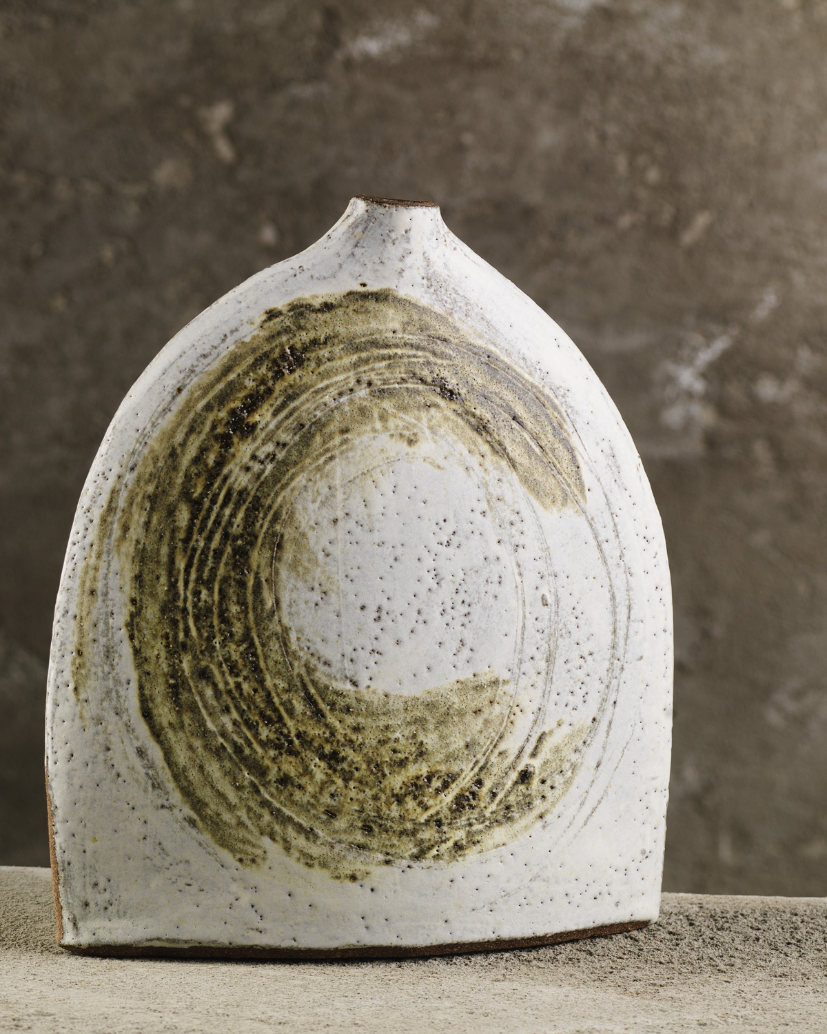 A minimalist ceramic sculpture with a rounded top and white base, decorated with abstract circular patterns in earthy tones, set against a neutral background.