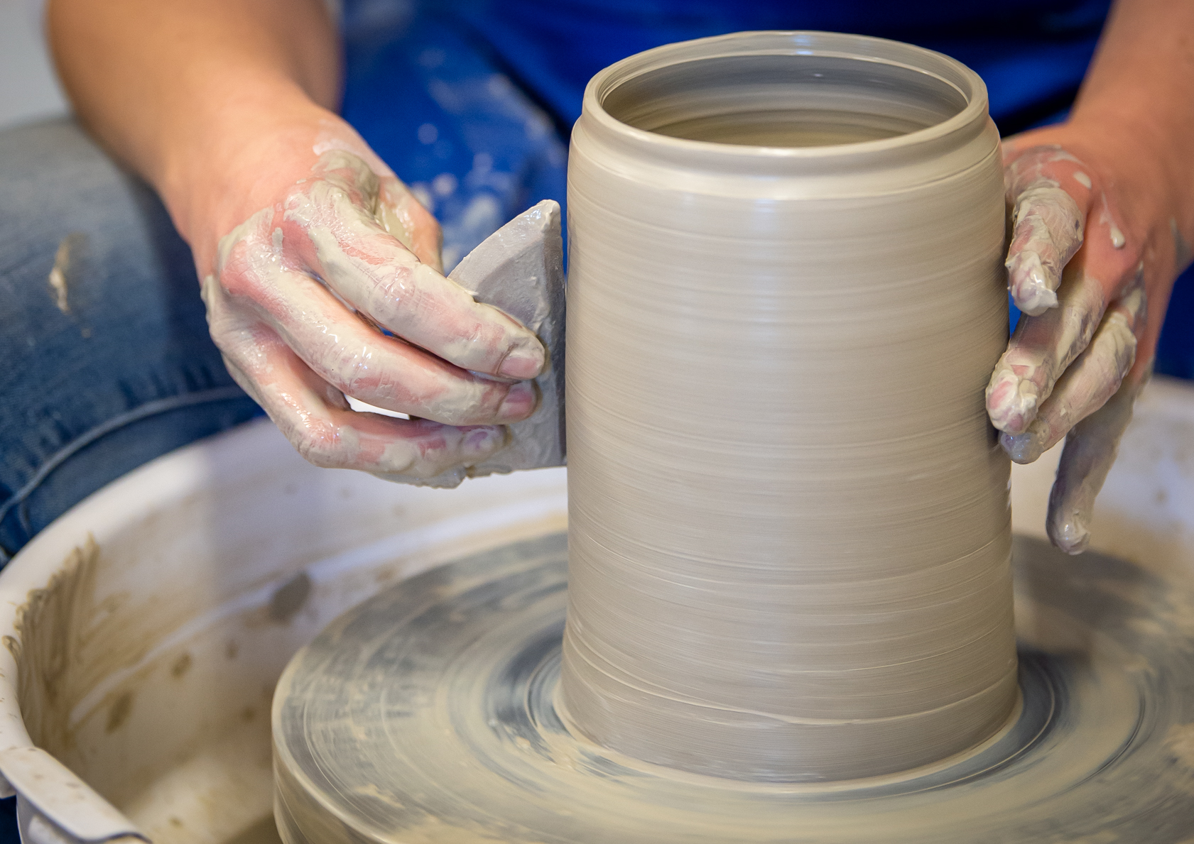 Person shaping a clay vase on a pottery wheel, with hands covered in clay.