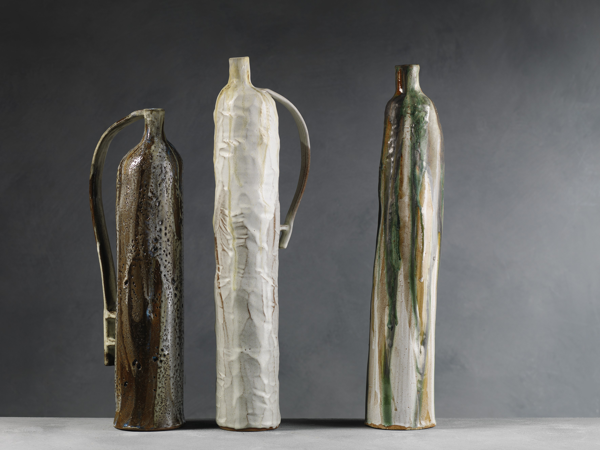 Three tall ceramic vases with different glazes and textures on a flat surface against a dark gray background.