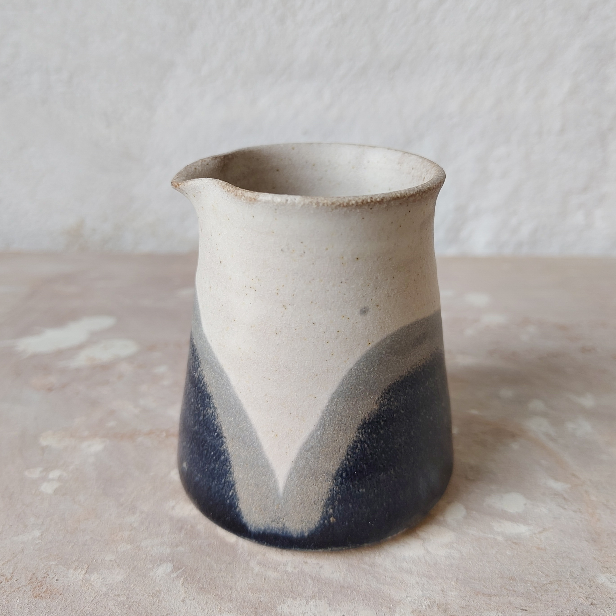 Close-up of a small beige ceramic vase with a flared opening, placed on a textured beige surface.