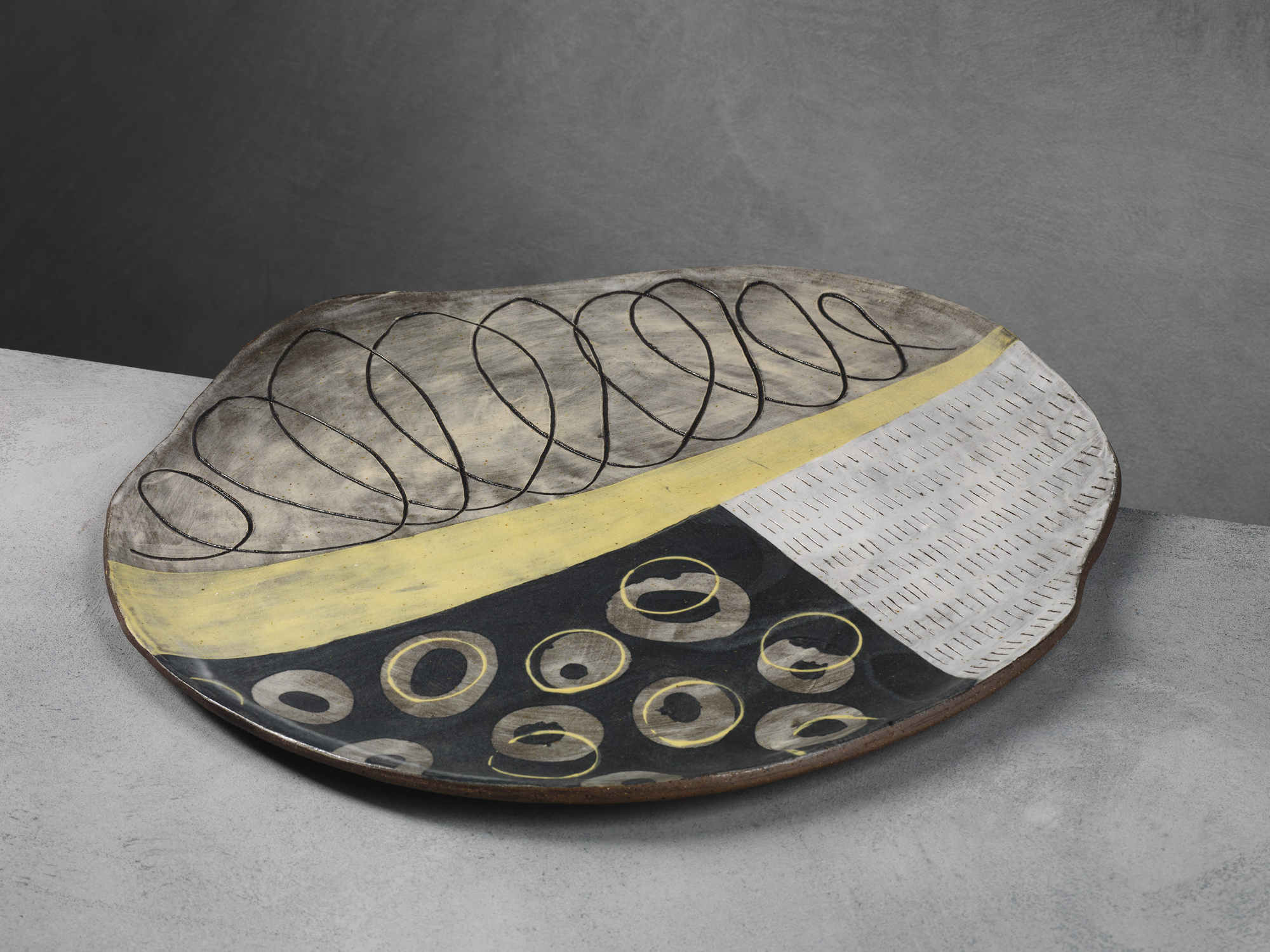 Decorative ceramic bowl with abstract black, yellow, and white patterns on a gray background.